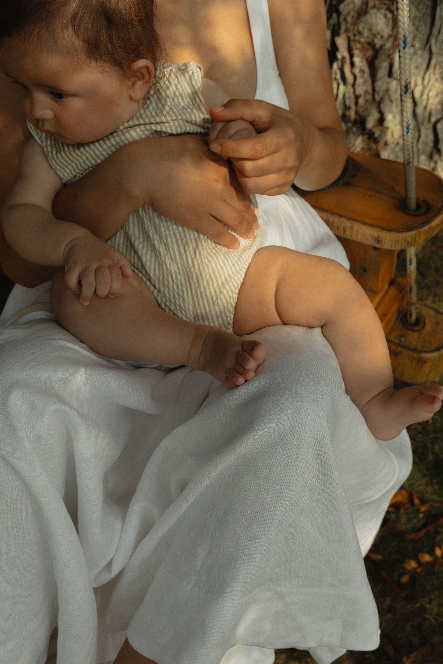 Close-up of a newborn baby resting on a mothers lap in a white dress outdoors.