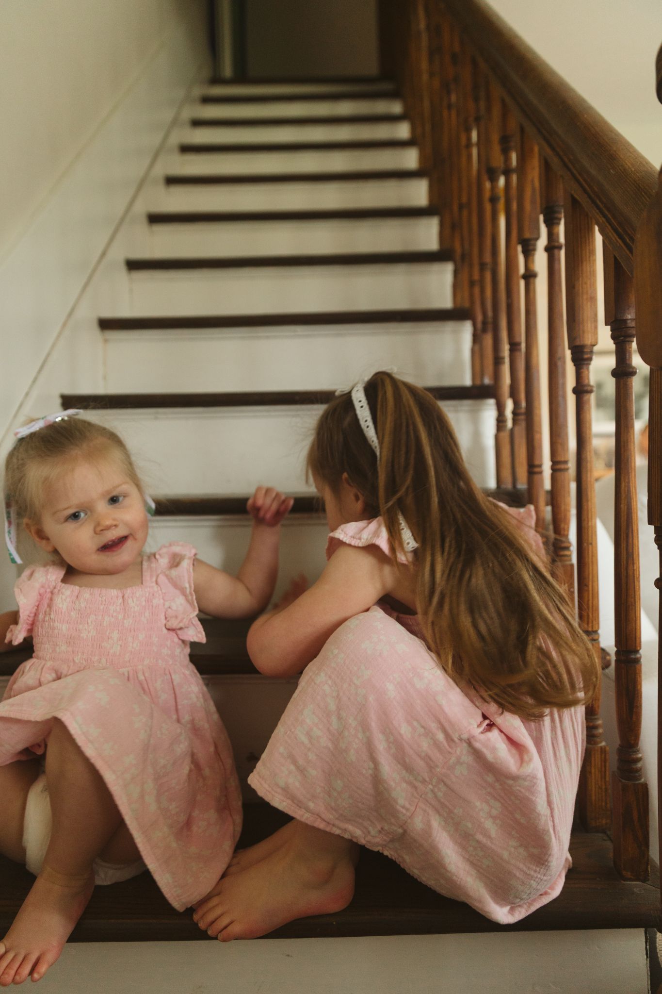 Two people in matching pink outfits sitting on wooden stairs.