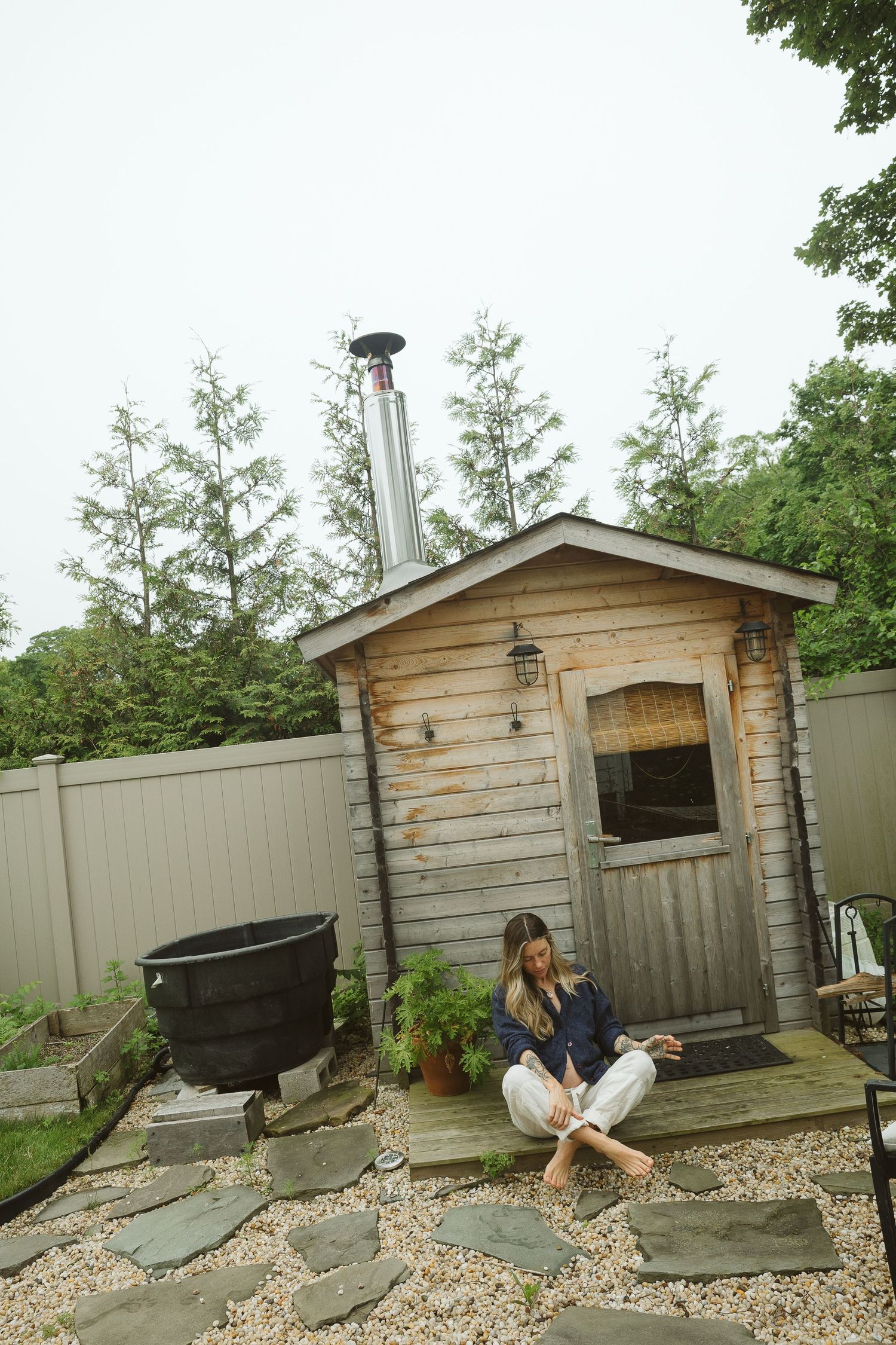Rustic wooden sauna or shed with stone path and metal pot in backyard garden.