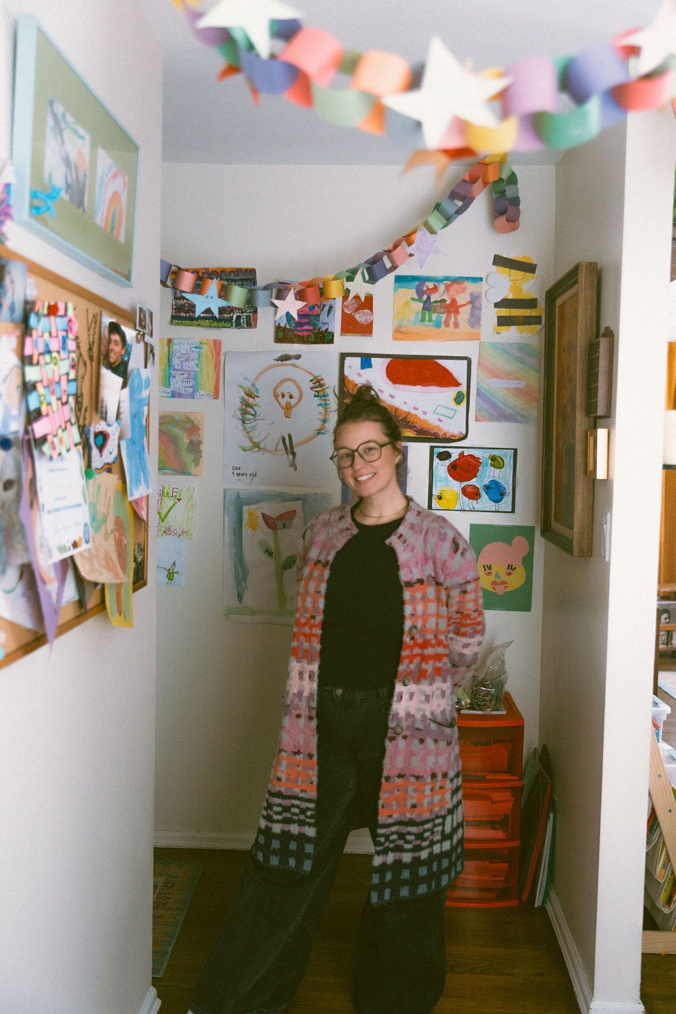 Woman in colorful cardigan standing in hallway covered with childrens artwork and paper garland.