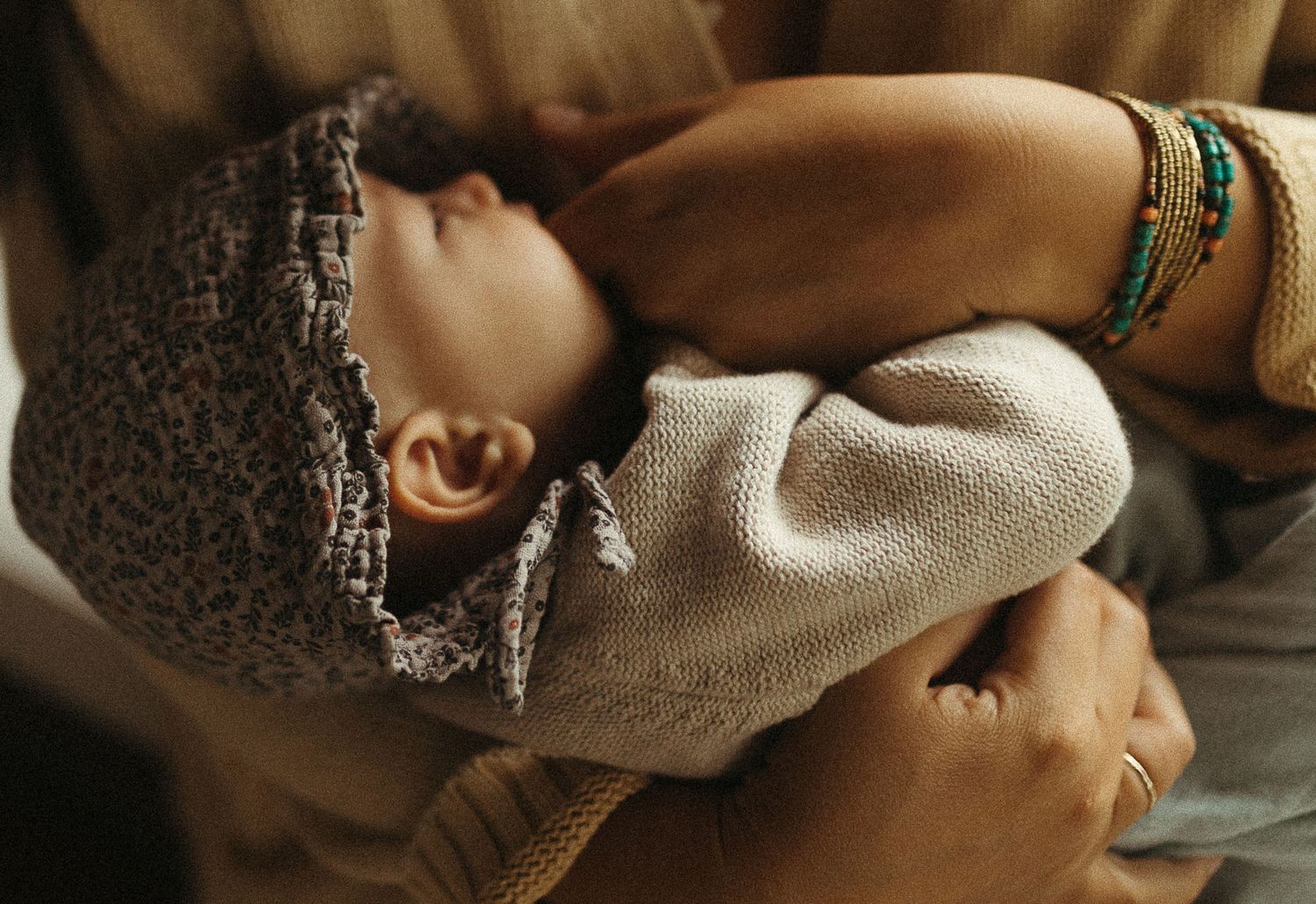 Close-up of newborn baby in floral bonnet being cradled in mother's arms with bracelets.