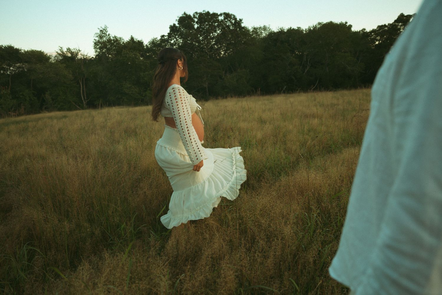 People in flowing white clothes move through a sunlit meadow during golden hour.