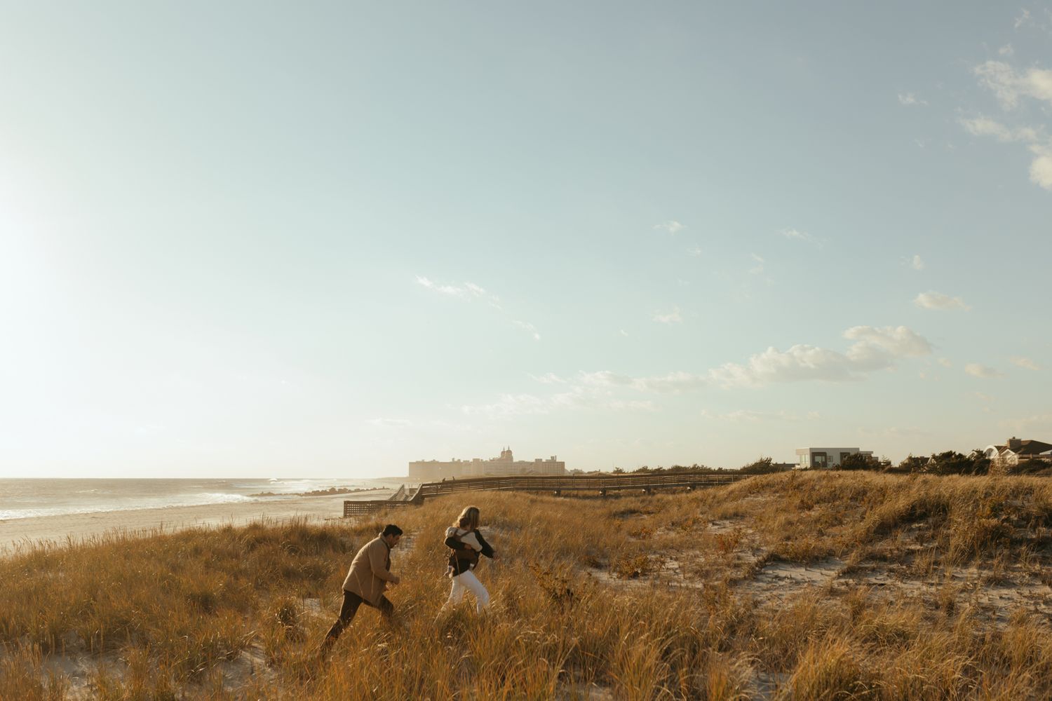 A group plays and laughs together in a field of tall golden grass during sunset.