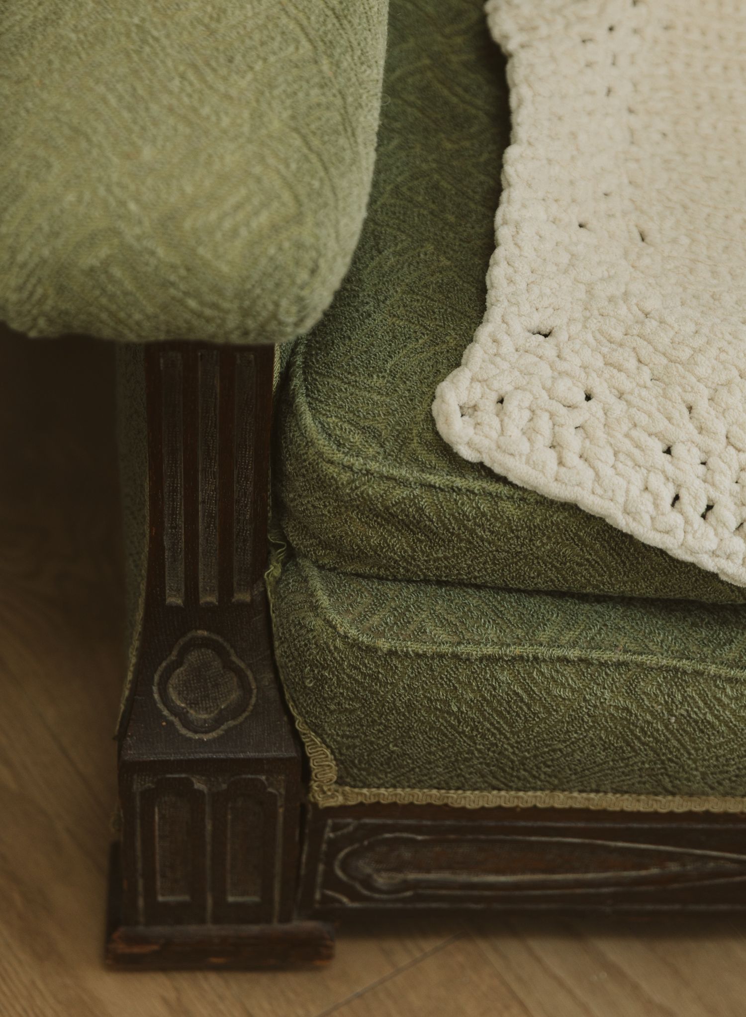 Close-up of green velvet couch cushion with white crochet throw blanket.