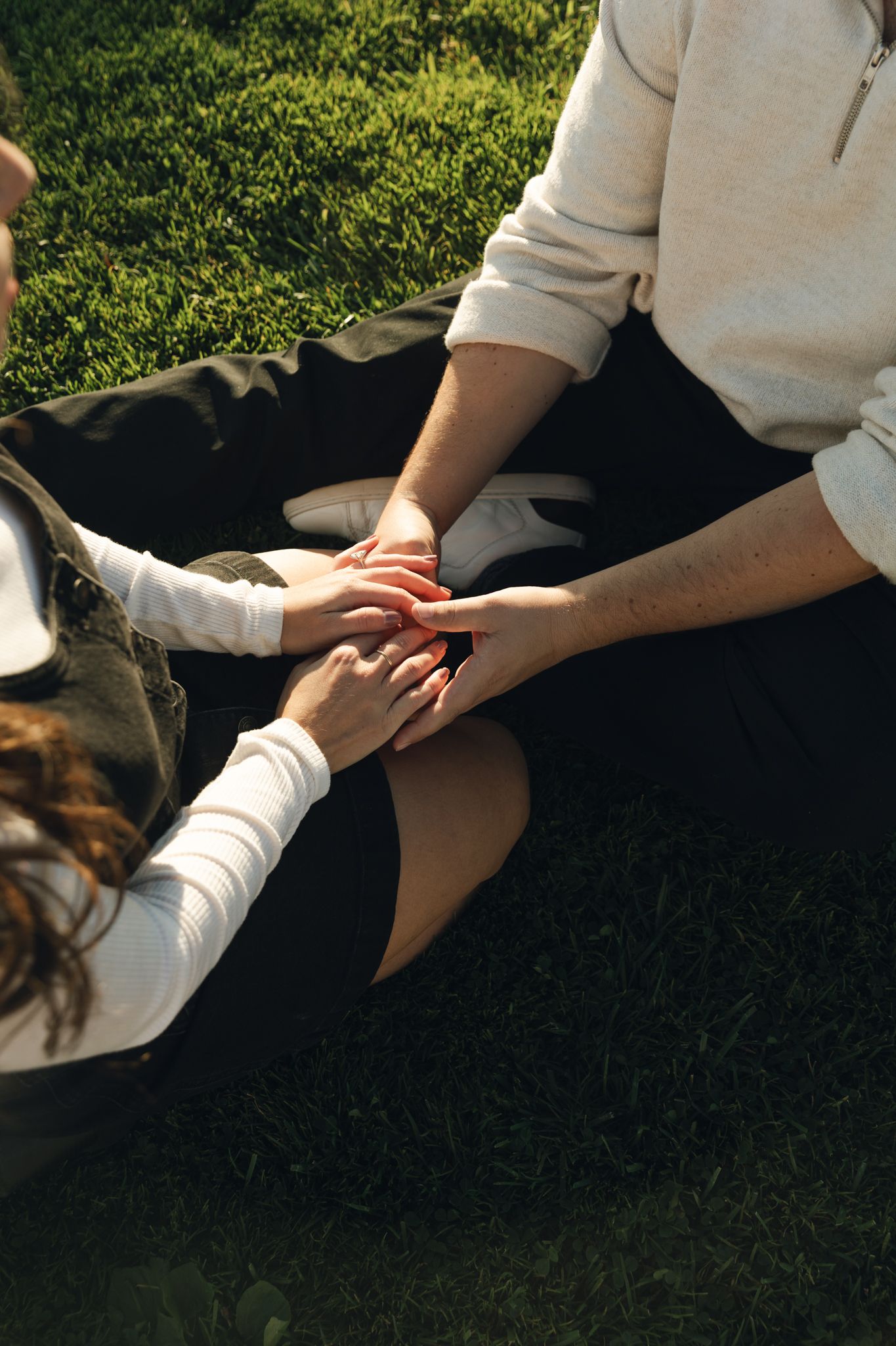 Close-up of hands reaching towards each other on grassy ground.