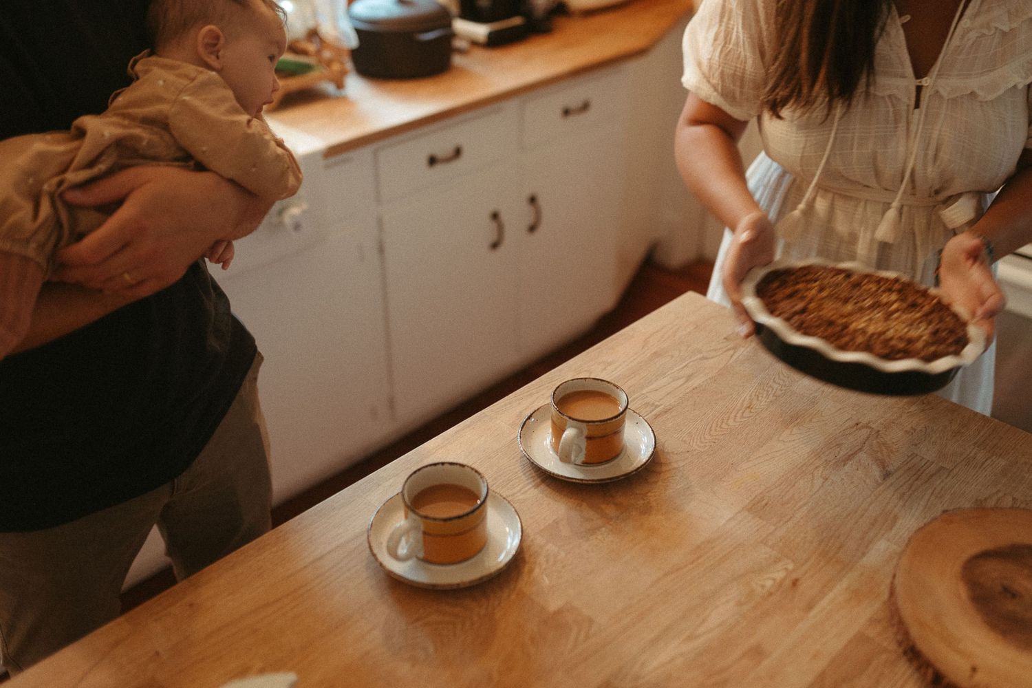 Warm gathering around a wooden table with coffee cups and desserts in a cozy kitchen setting.