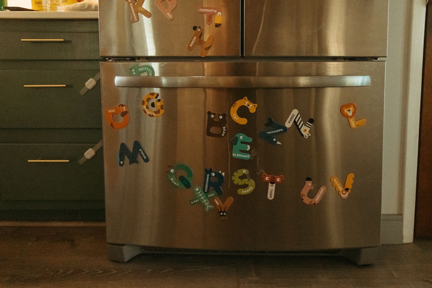 Stainless steel refrigerator decorated with colorful magnetic letters and artwork.