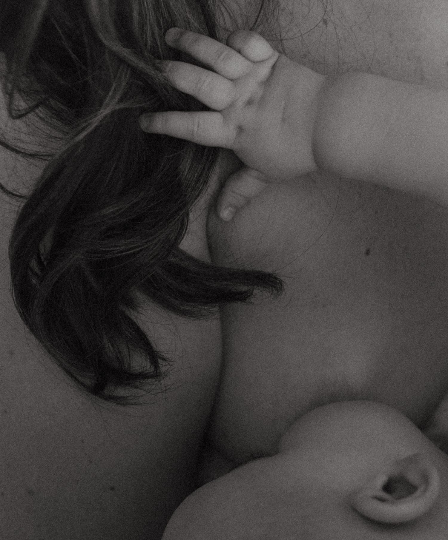 Black and white close-up of baby reaching tiny hand up to touch mothers dark hair tenderly.