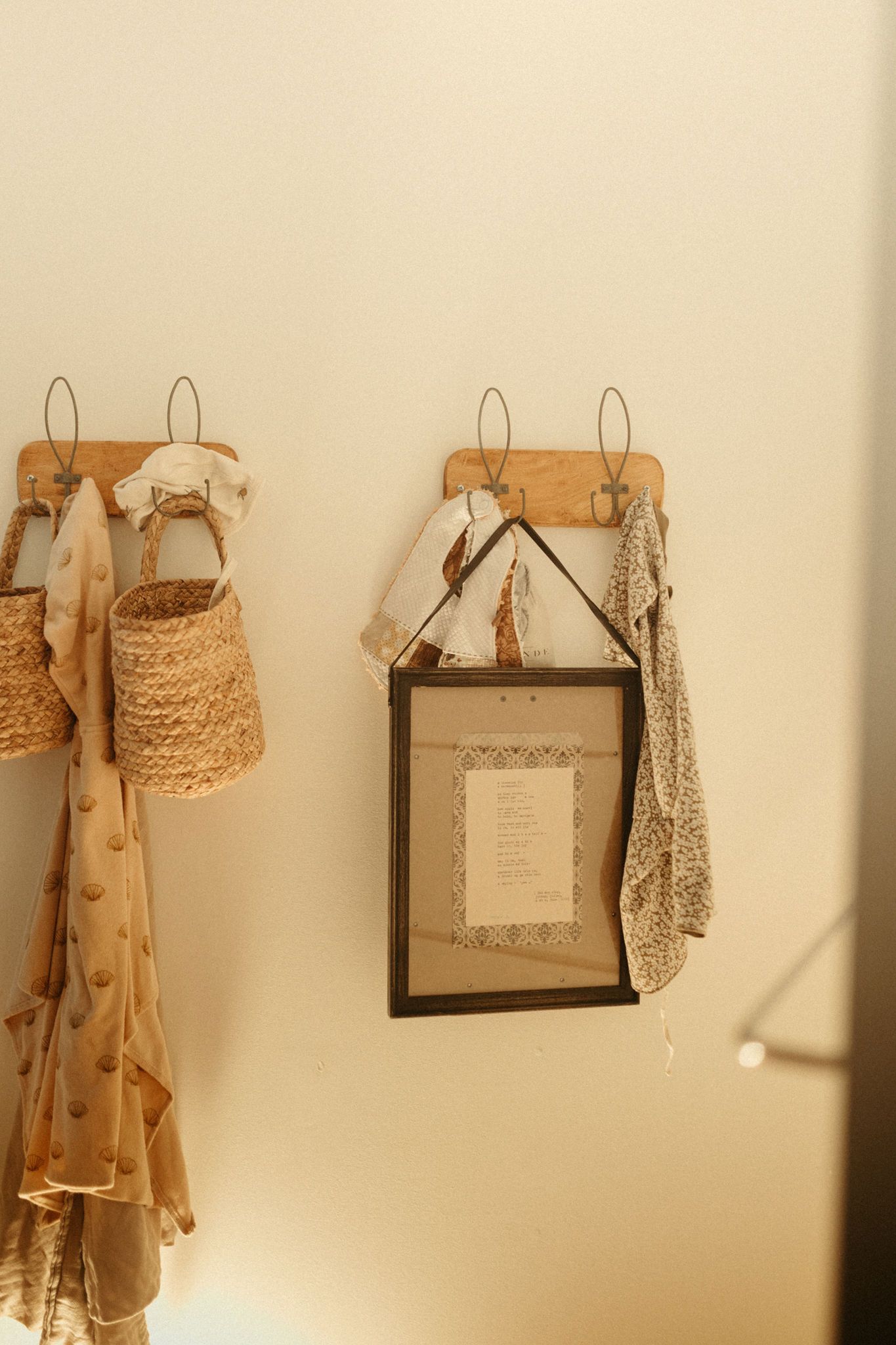 Woven baskets and a framed document hang on rustic wall hooks against a cream-colored wall.