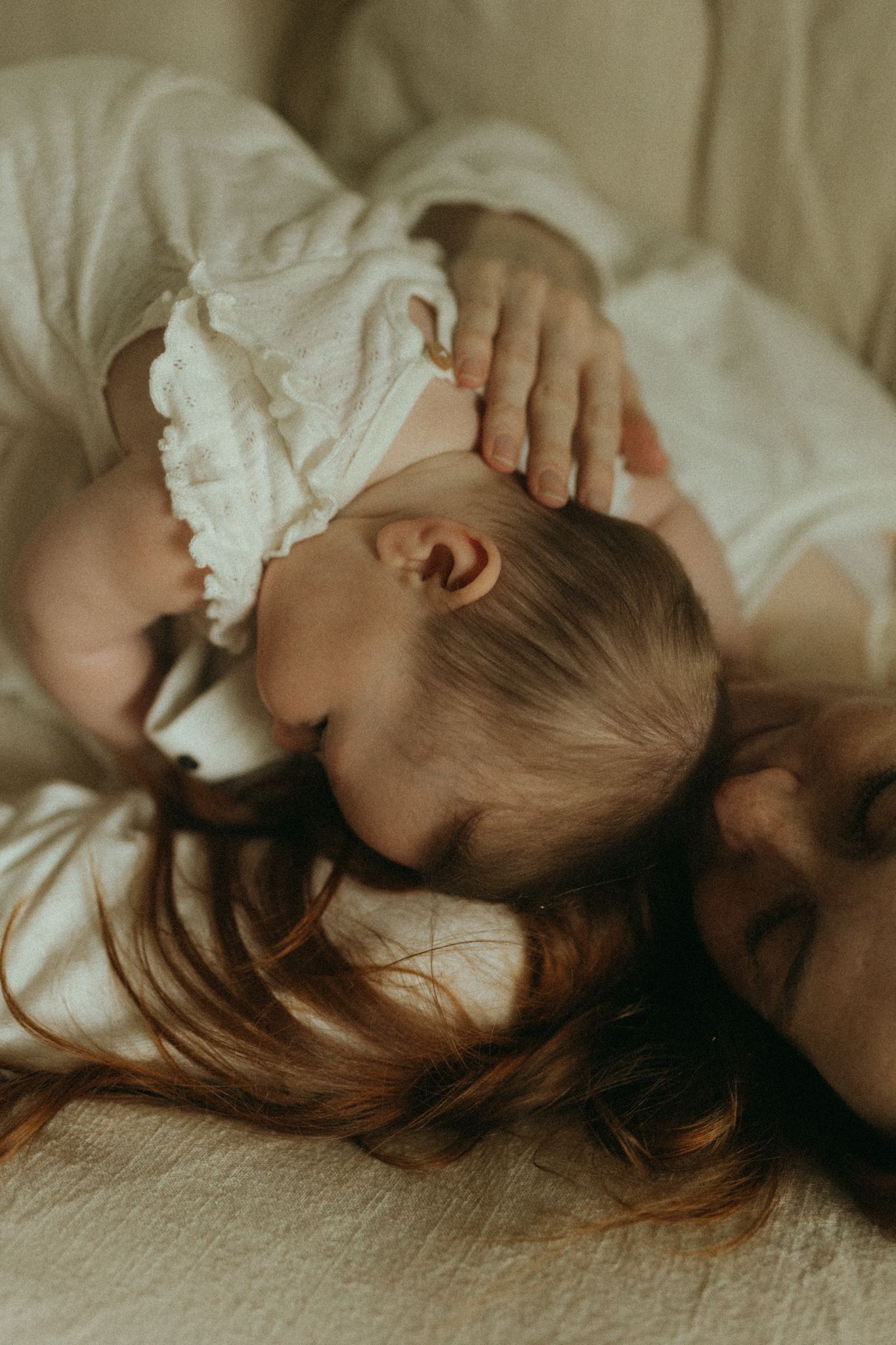 A mother and baby lying together on a bed, both dressed in white, sharing a tender close moment.