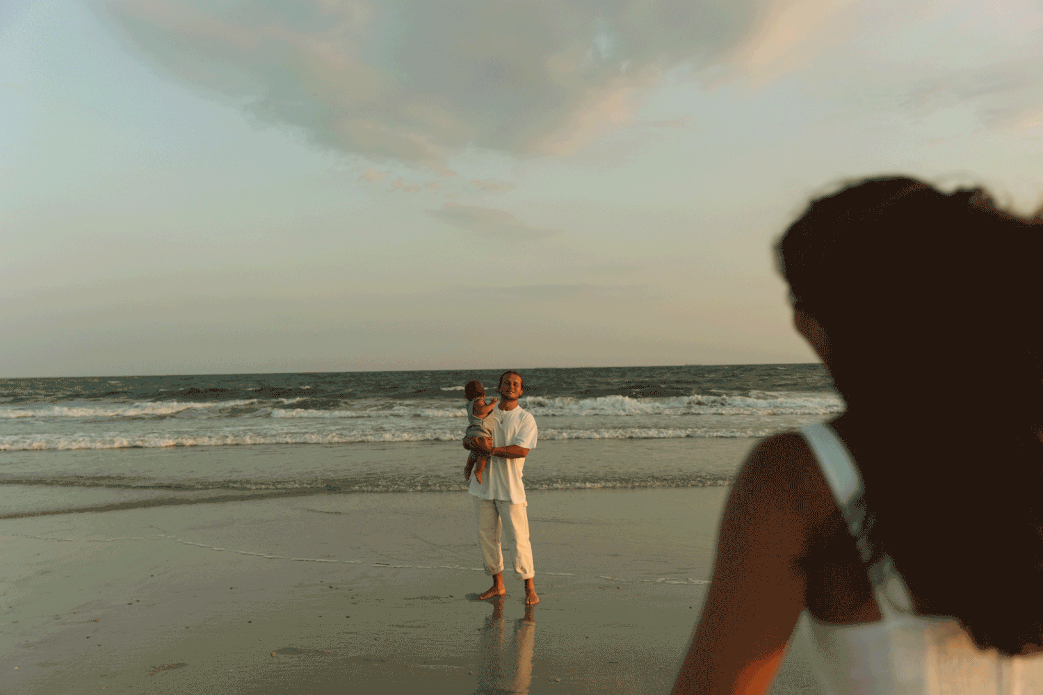 Mom twirling towards baby and father at the ocean.