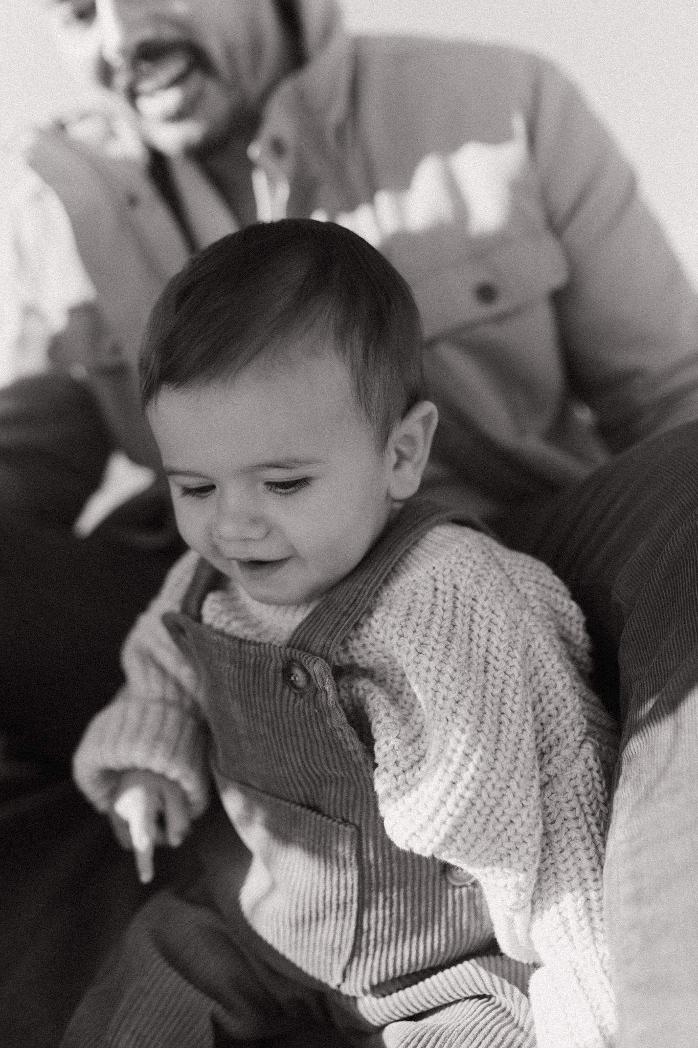 A candid black and white portrait of a young child wearing a knit sweater and corduroy overalls.