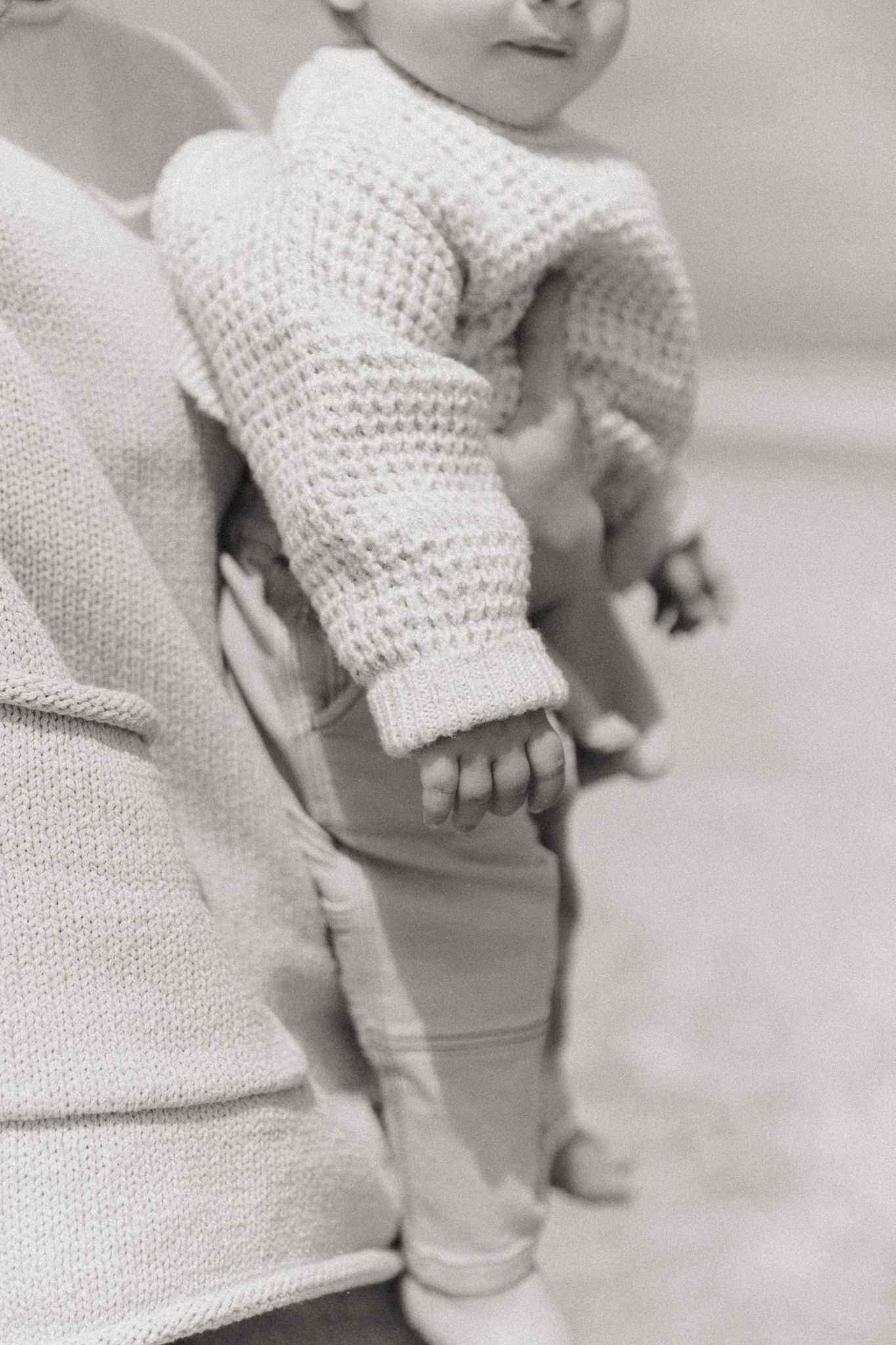 Close up view of small hands and cream knit sweater details.