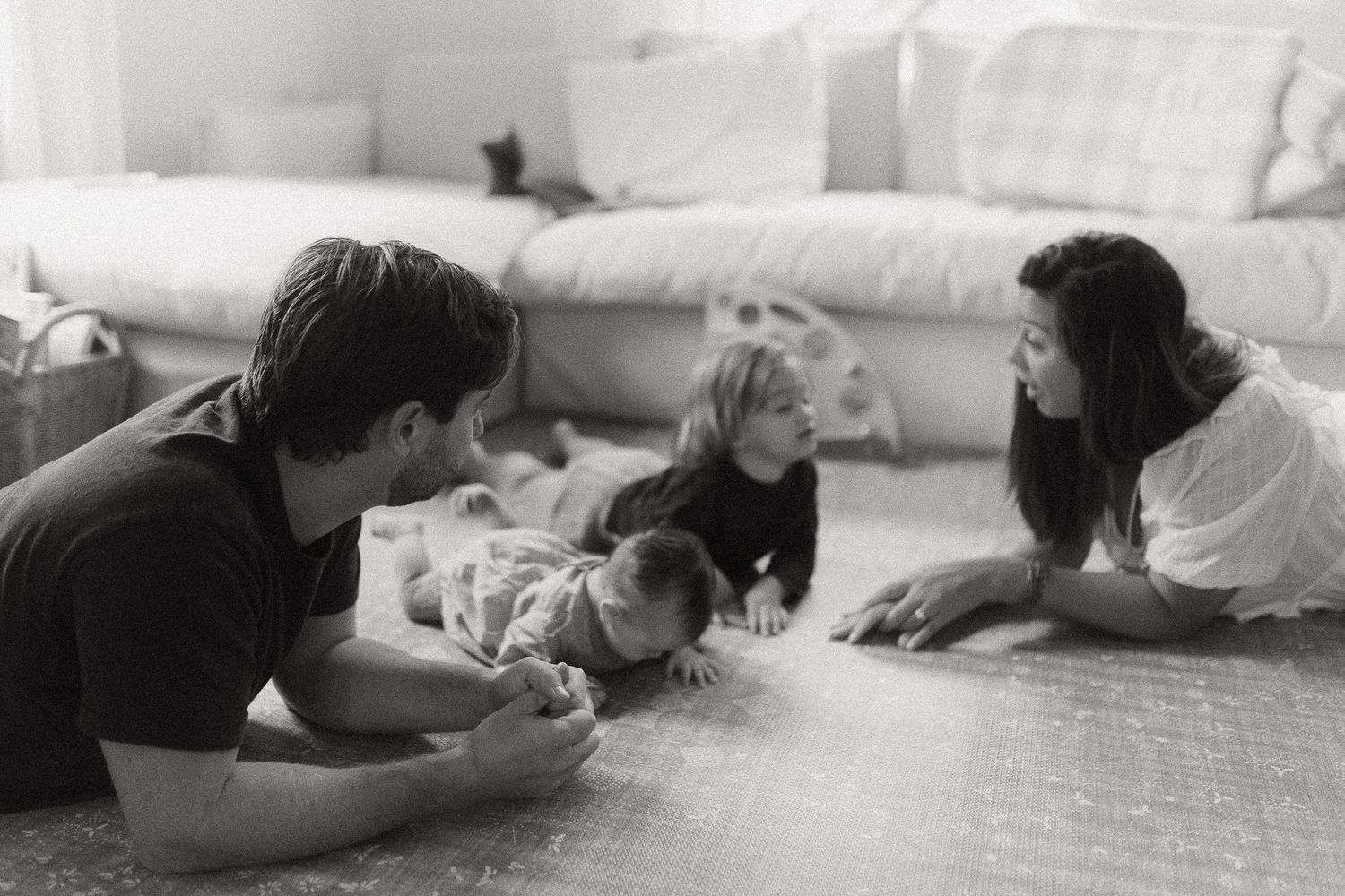 Black and white family photo of parents and two children lying together on a cozy living room floor.