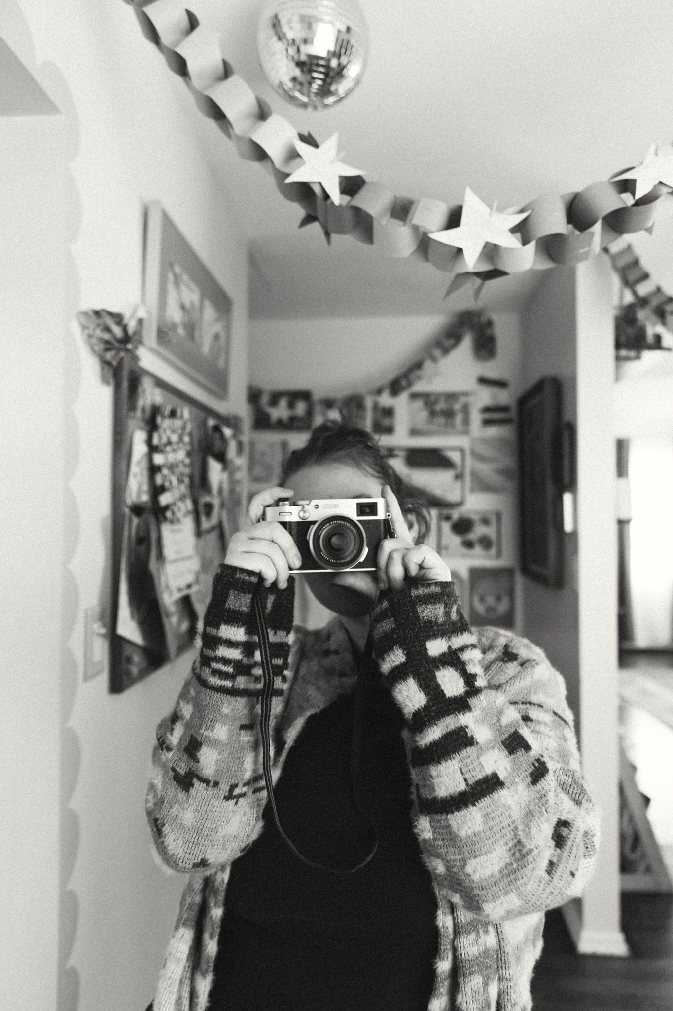 Black and white photo of person holding vintage camera in decorated hallway with star garland.