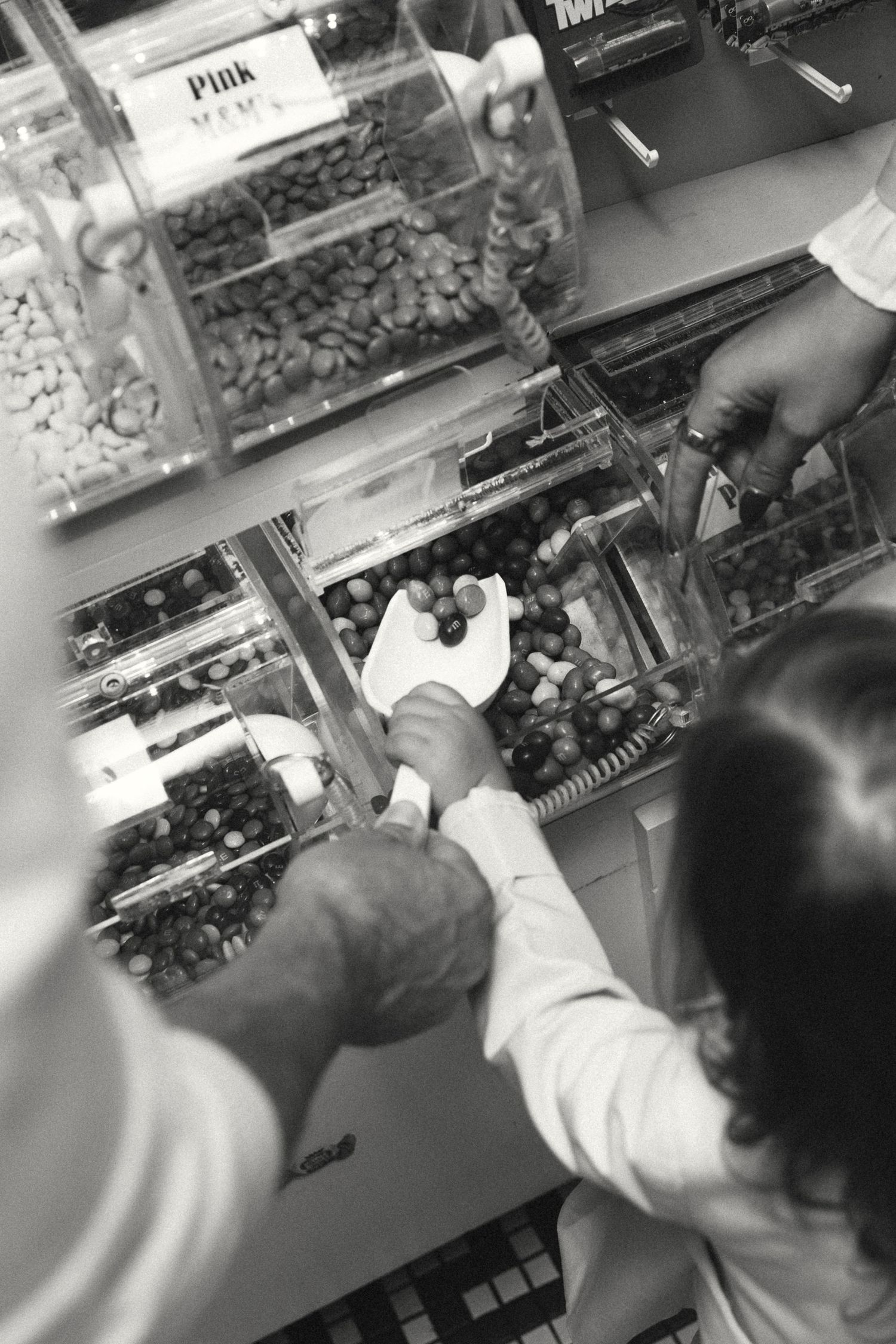 Close-up view of hands reaching for candy in bulk bins at a store.