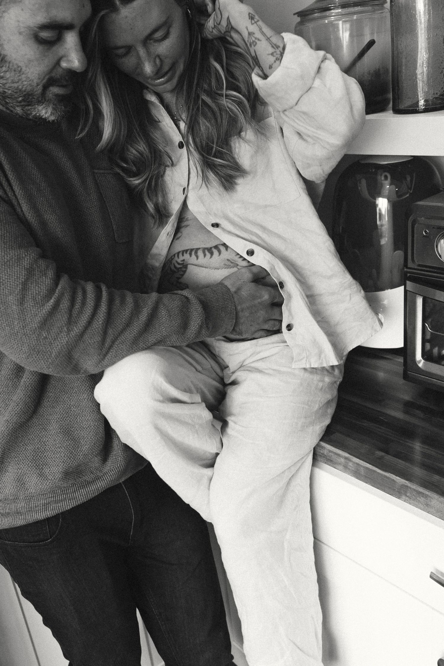 Black and white intimate maternity photo in kitchen setting.