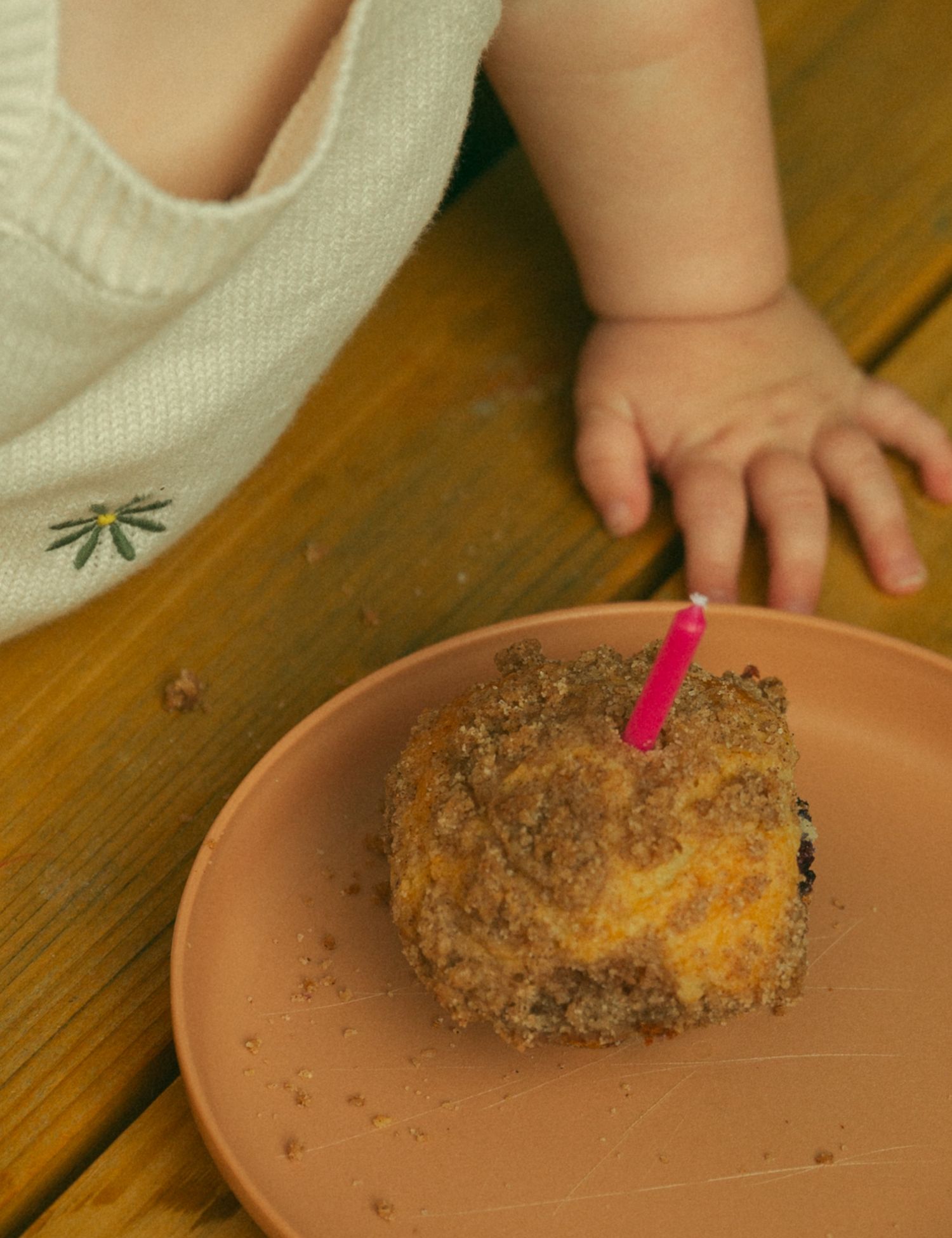 Pink birthday candle stuck in a crumb-covered dessert on a terra cotta plate.