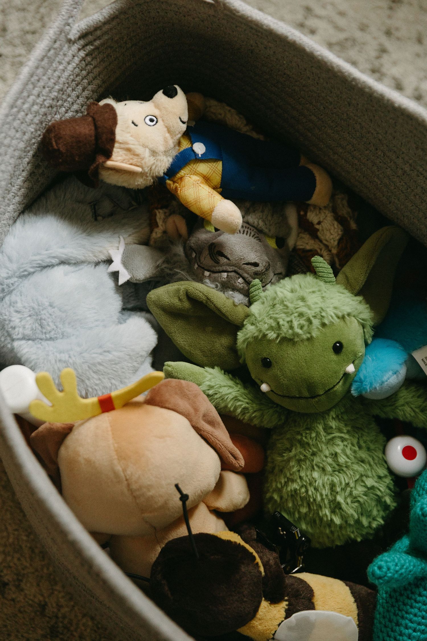 Collection of colorful stuffed animal toys including green dragon and moose in round fabric basket.