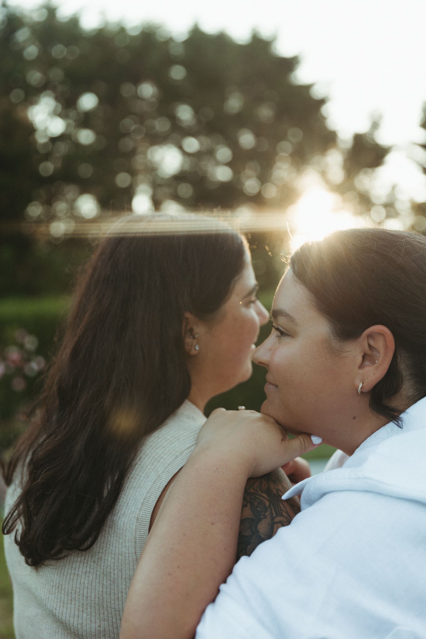 Two women nearly kissing in intimate close-up portrait with warm bokeh sunlight background.