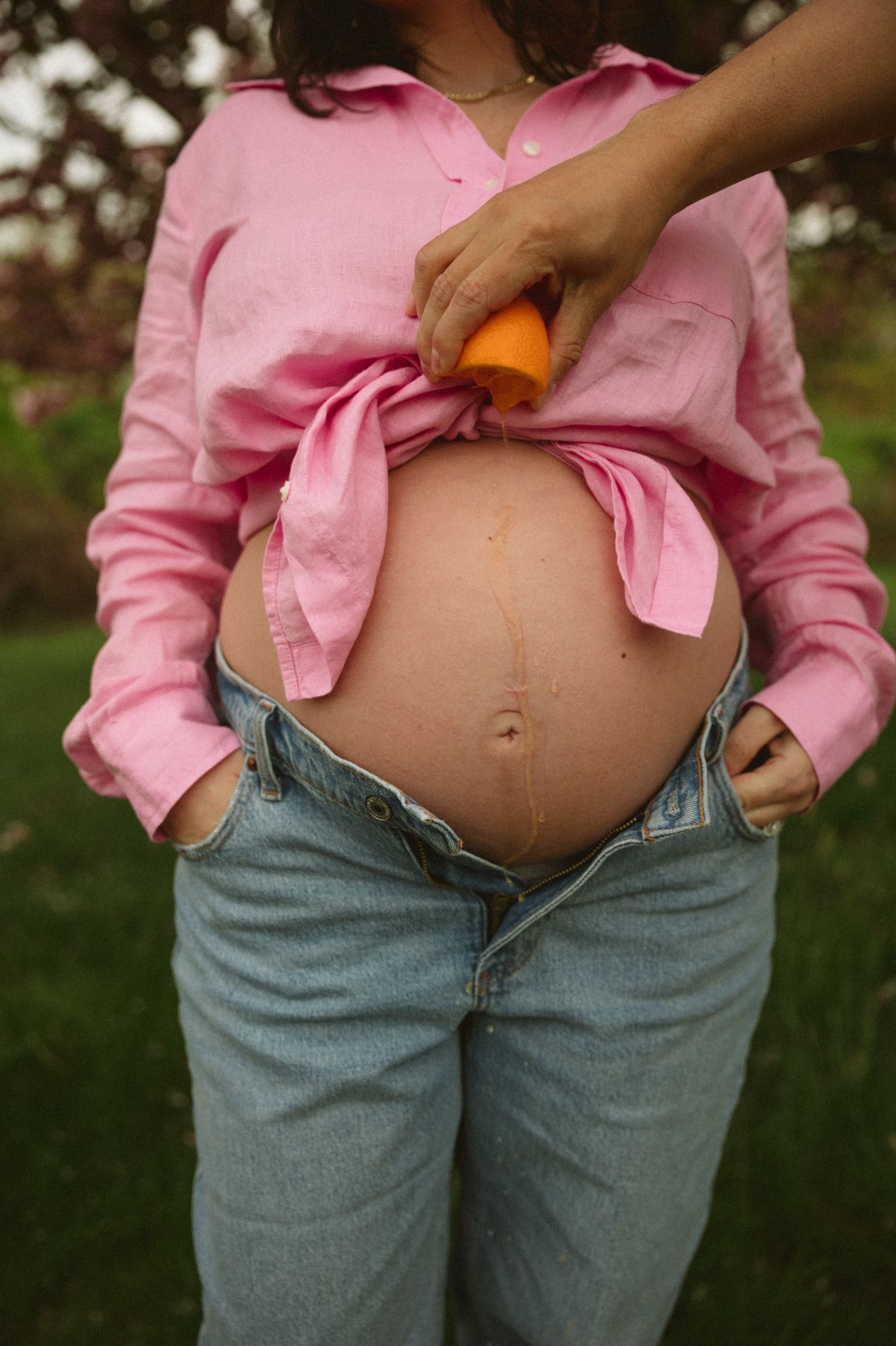 Pregnant belly shown under pink button-up shirt and denim jeans.