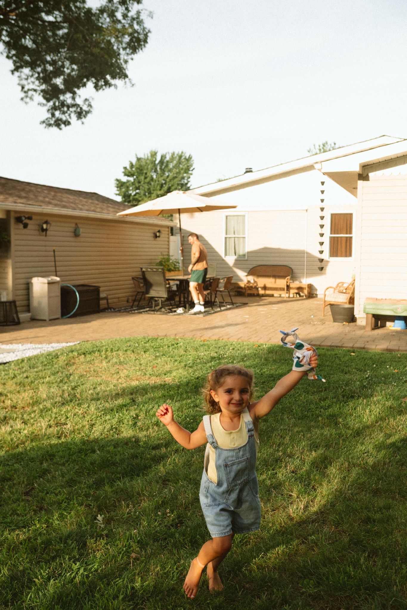 Child in overalls playing in a backyard during golden hour with houses in background.
