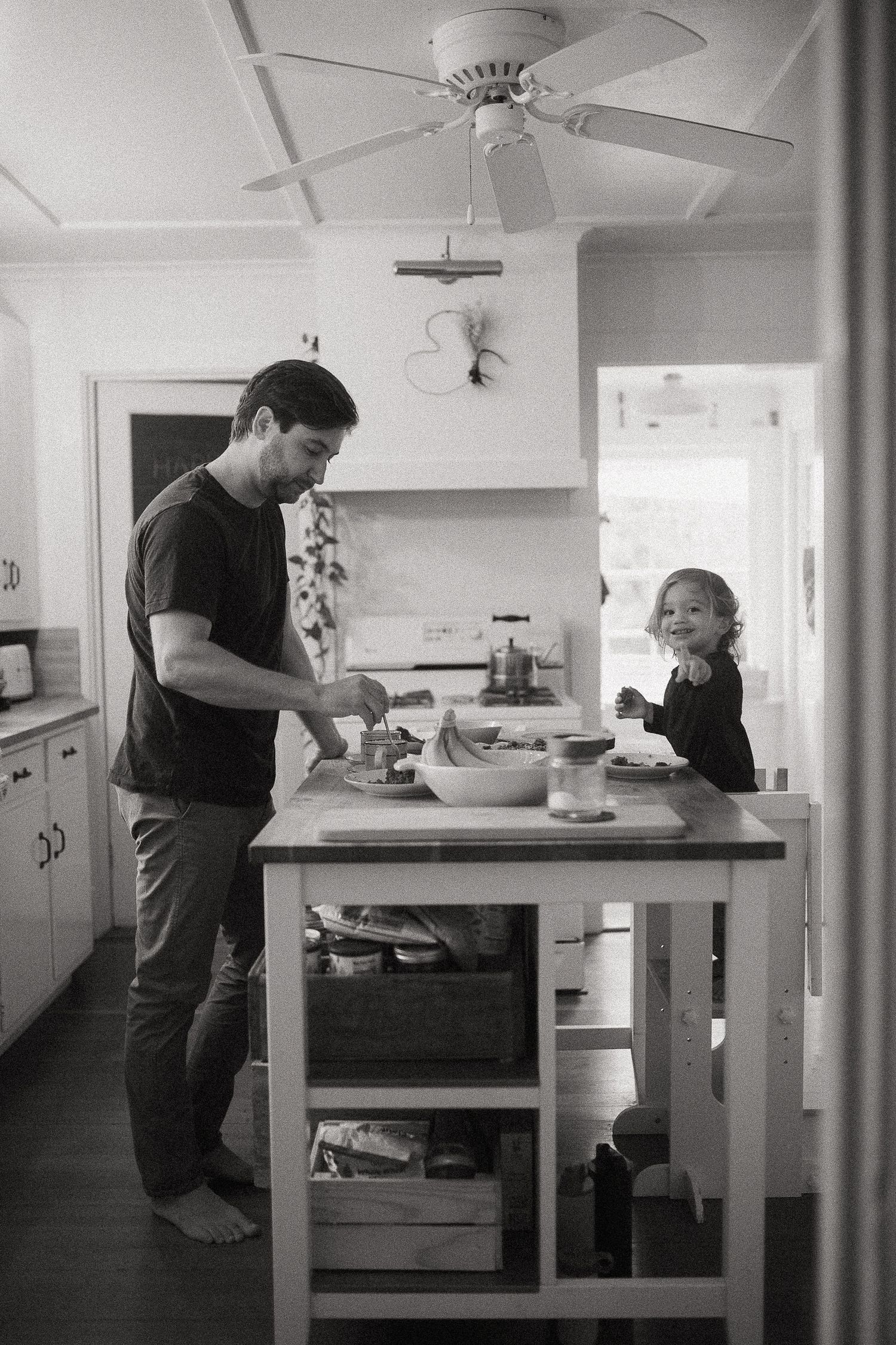 Black and white photo of a kitchen interior with people preparing food at countertops.