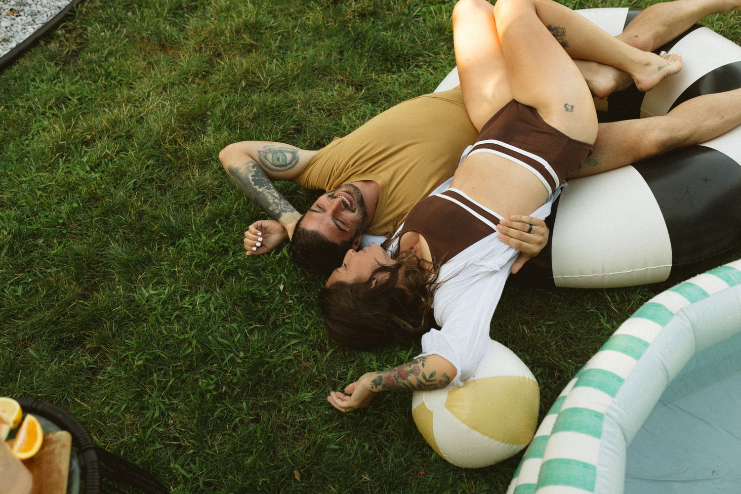 People relaxing on grass near an inflatable pool on a sunny day.