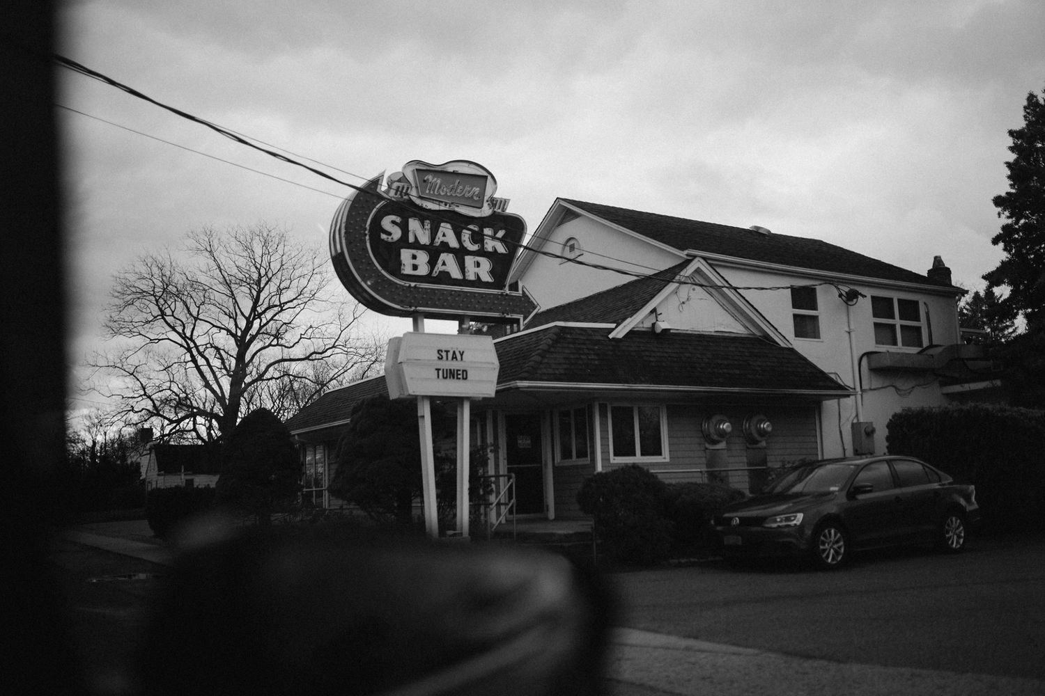 Black and white storefront signs and buildings line a commercial street at dusk.