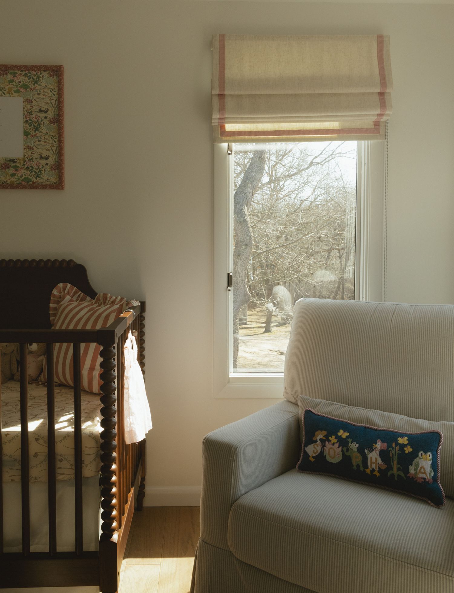 Cozy nursery corner with gray couch and window letting in natural light.