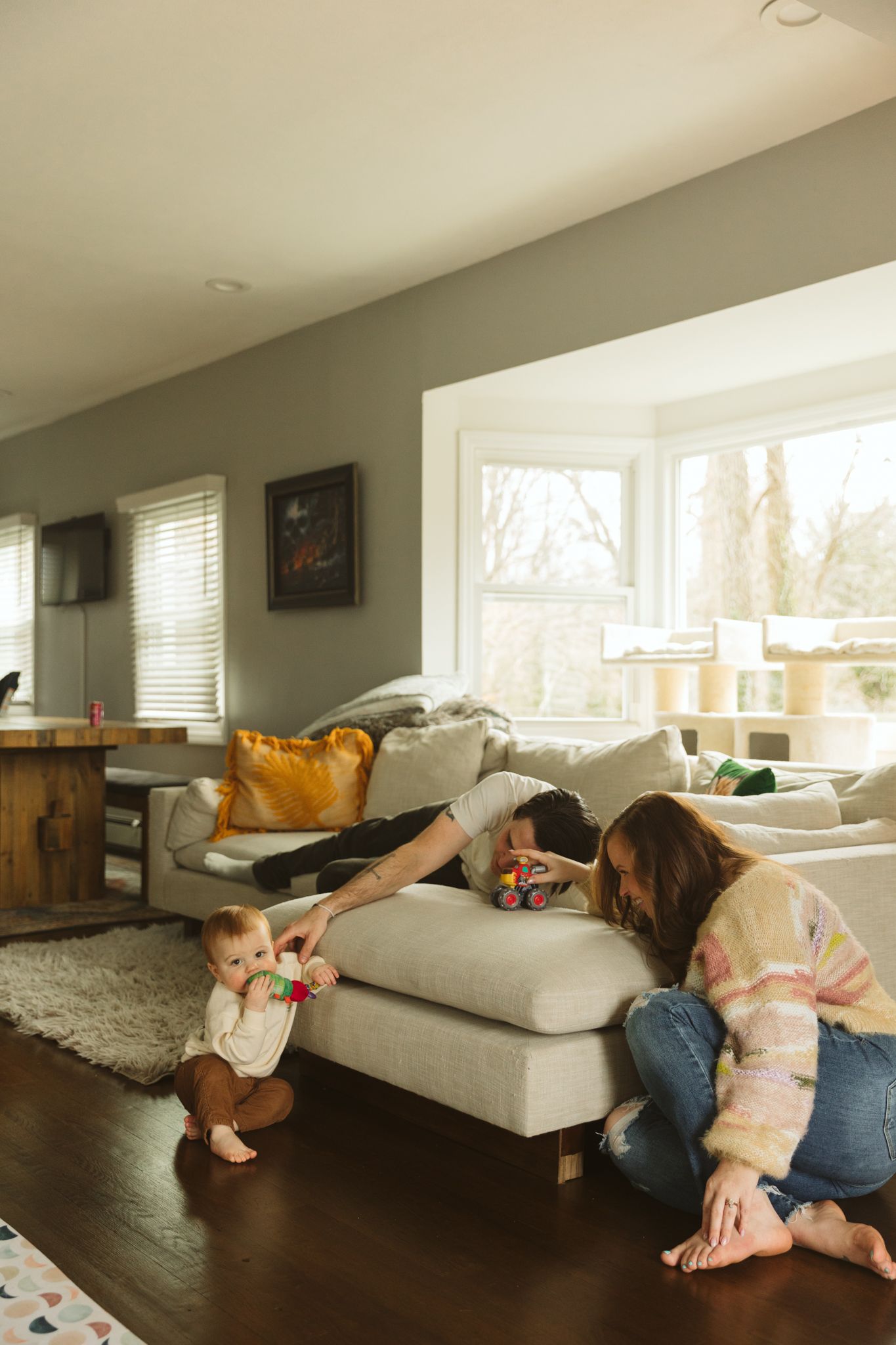 A cozy living room scene with a comfortable gray sectional sofa and large bay window letting in natural light.