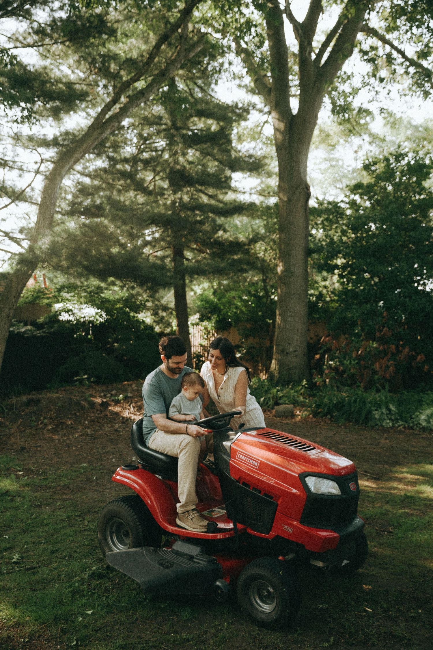A sequence showing people riding a red lawn tractor in a wooded backyard.
