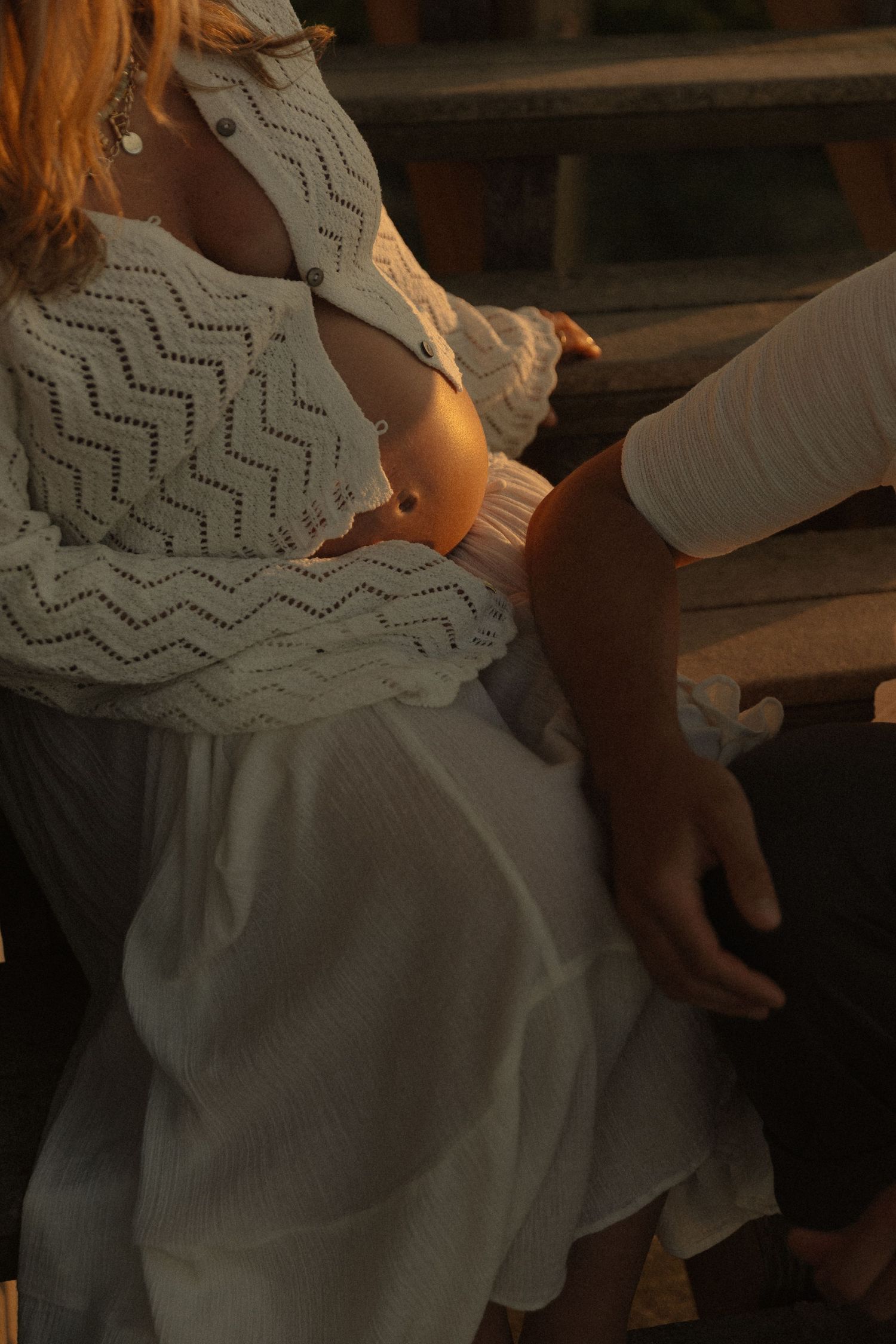 Woman in white lace top and skirt sitting beside a man at golden hour, warm sunset light casting a romantic glow.