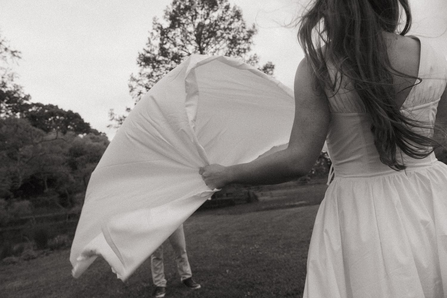 Black and white photo of a bride in a flowing white dress caught by the wind outdoors.