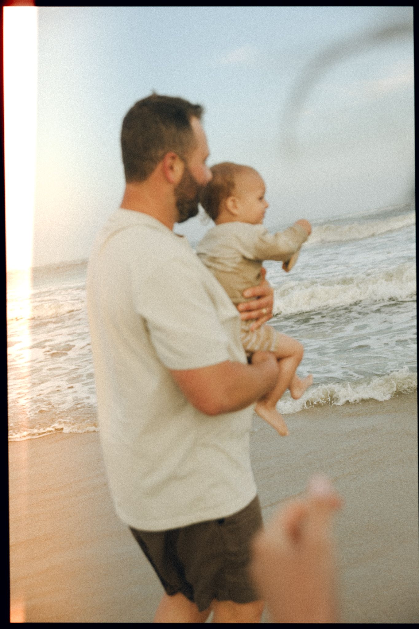 Parent and child watching ocean waves at sunset on beach.