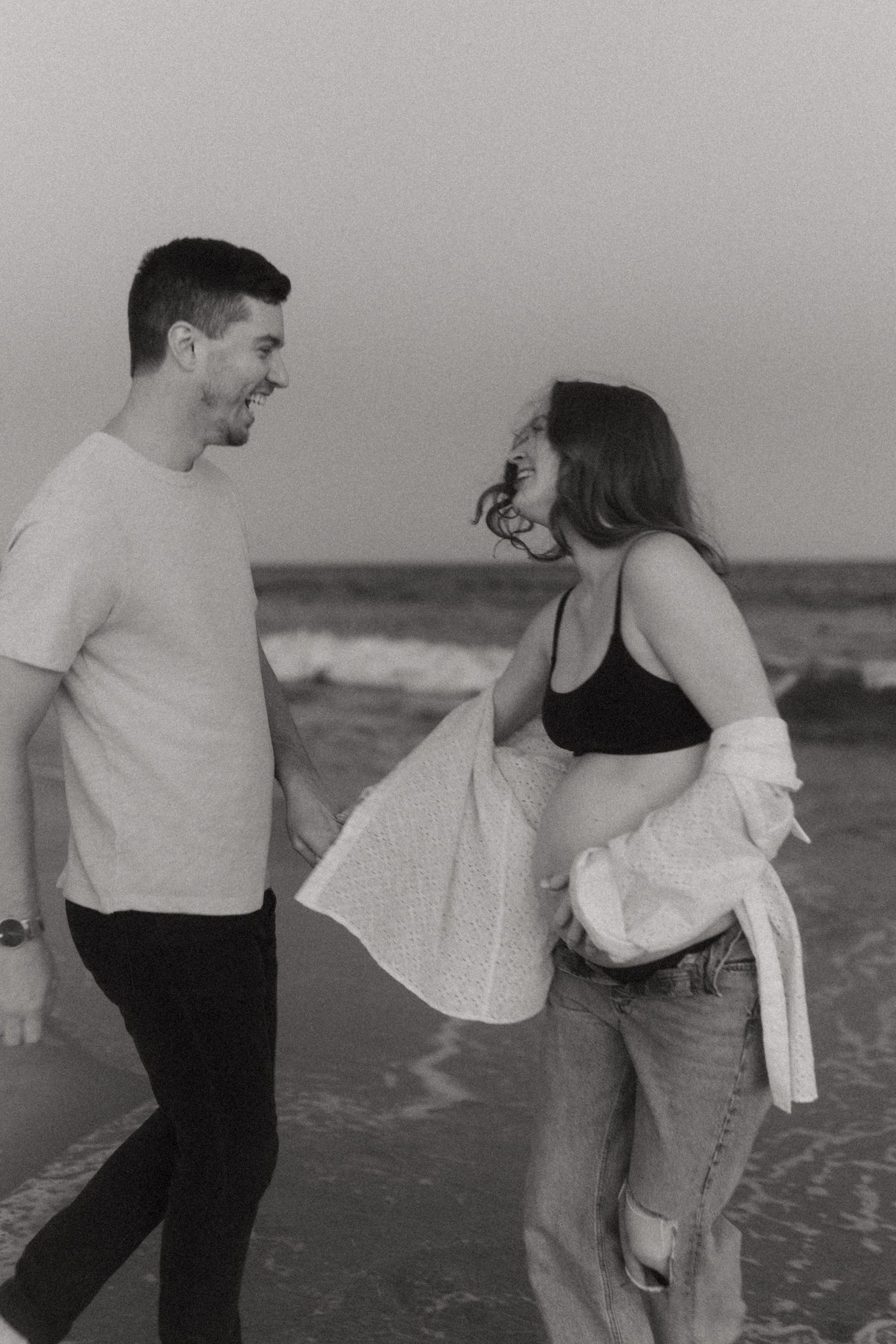 A couple shares a joyful dance moment on the beach in black and white.