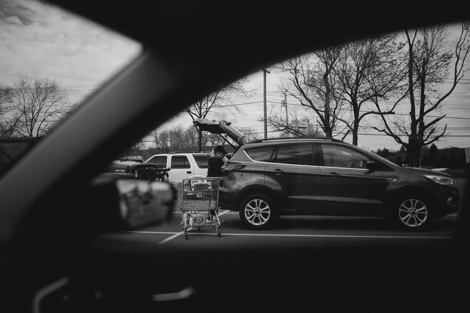 A shopping cart viewed through a car window in a parking lot.