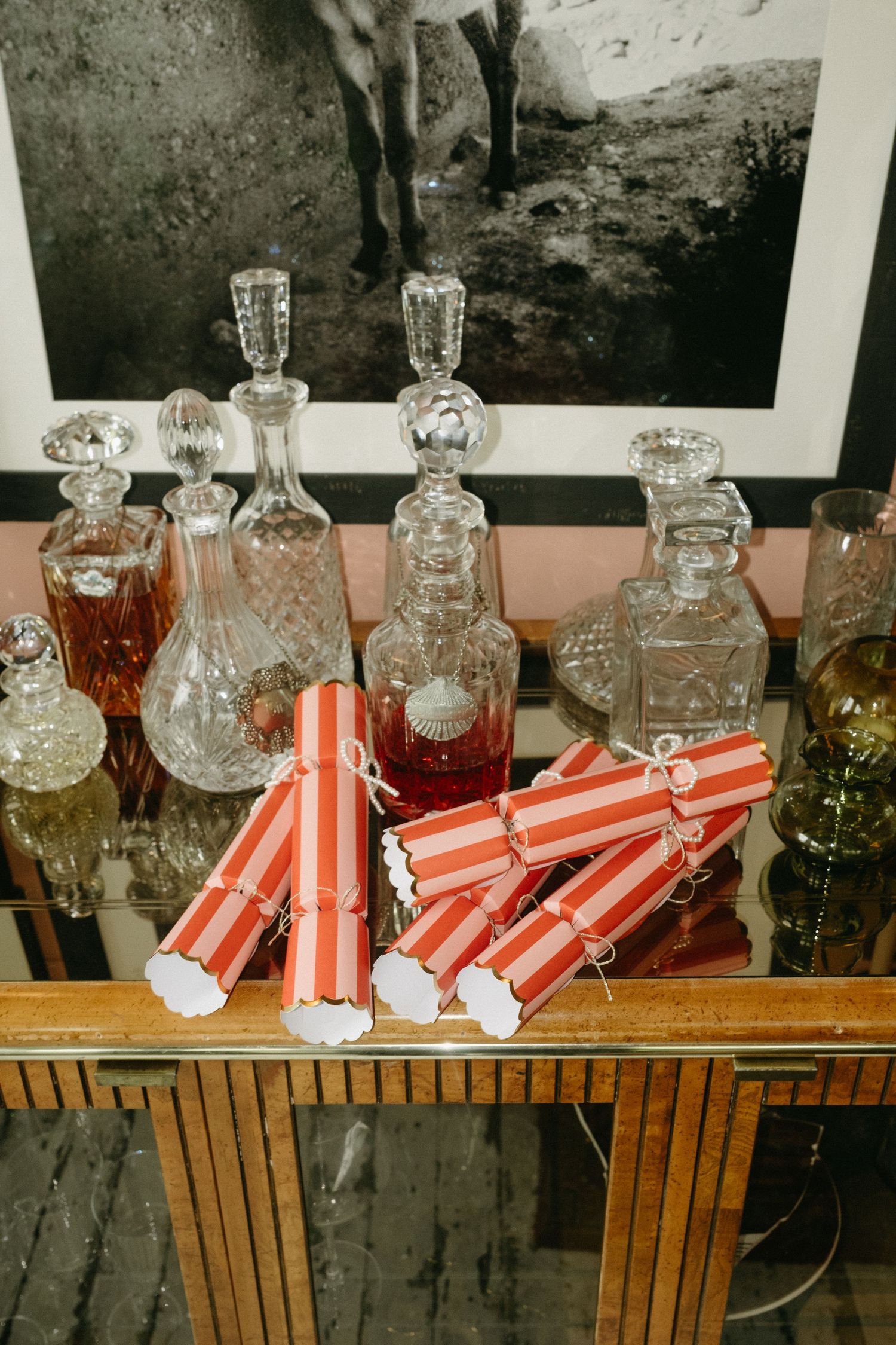 Crystal decanters with colorful liquors displayed on a glass table alongside red and white striped Christmas crackers.
