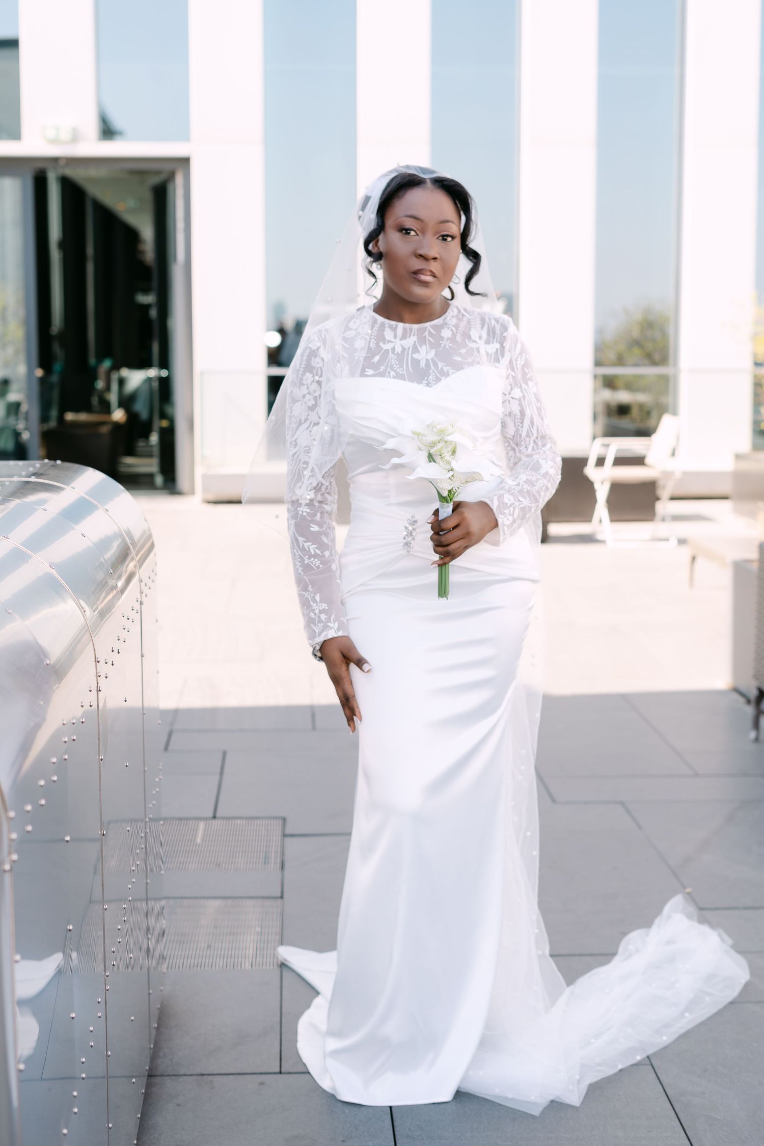 Beautiful Black bride in a white lace long-sleeve wedding dress holding a floral bouquet outdoors.