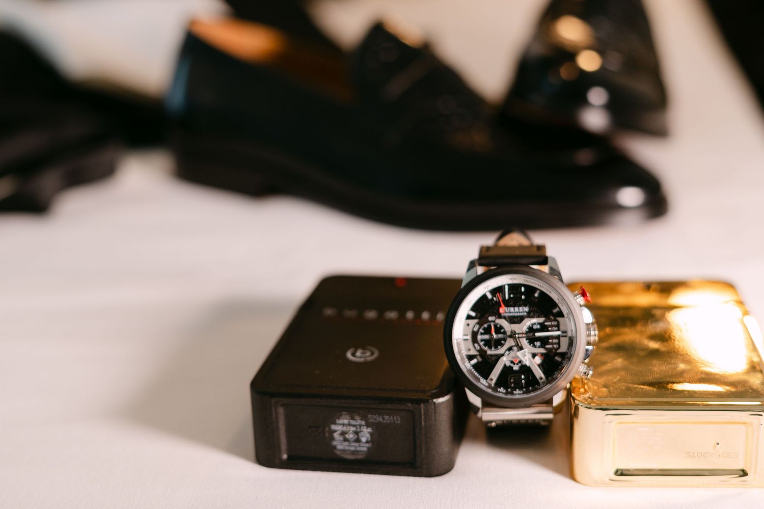 Luxury Fossil chronograph watch with leather strap beside gold box and black dress shoes.