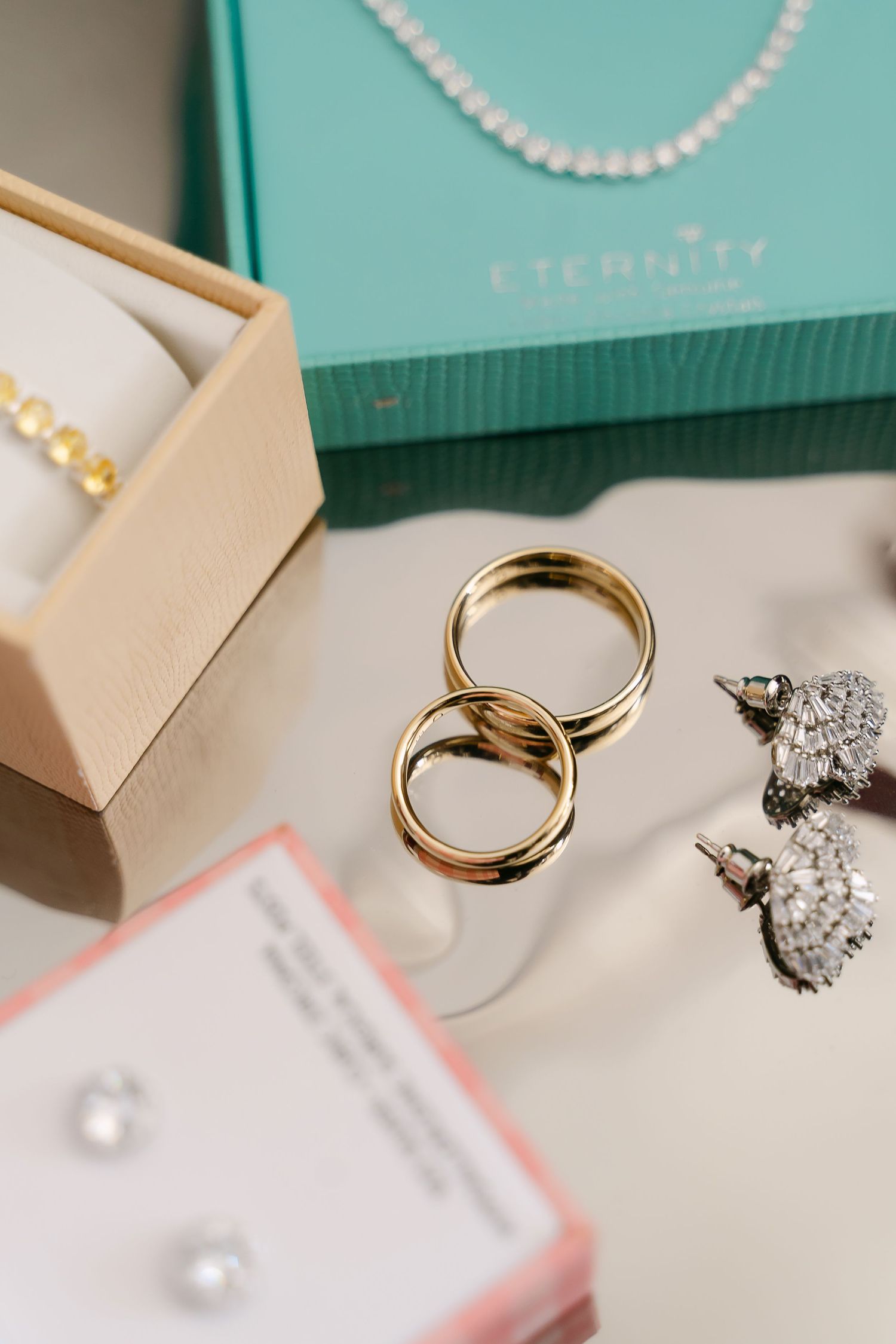 Gold wedding bands, pearl earrings, and diamond earrings displayed with an Eternity jewelry box.