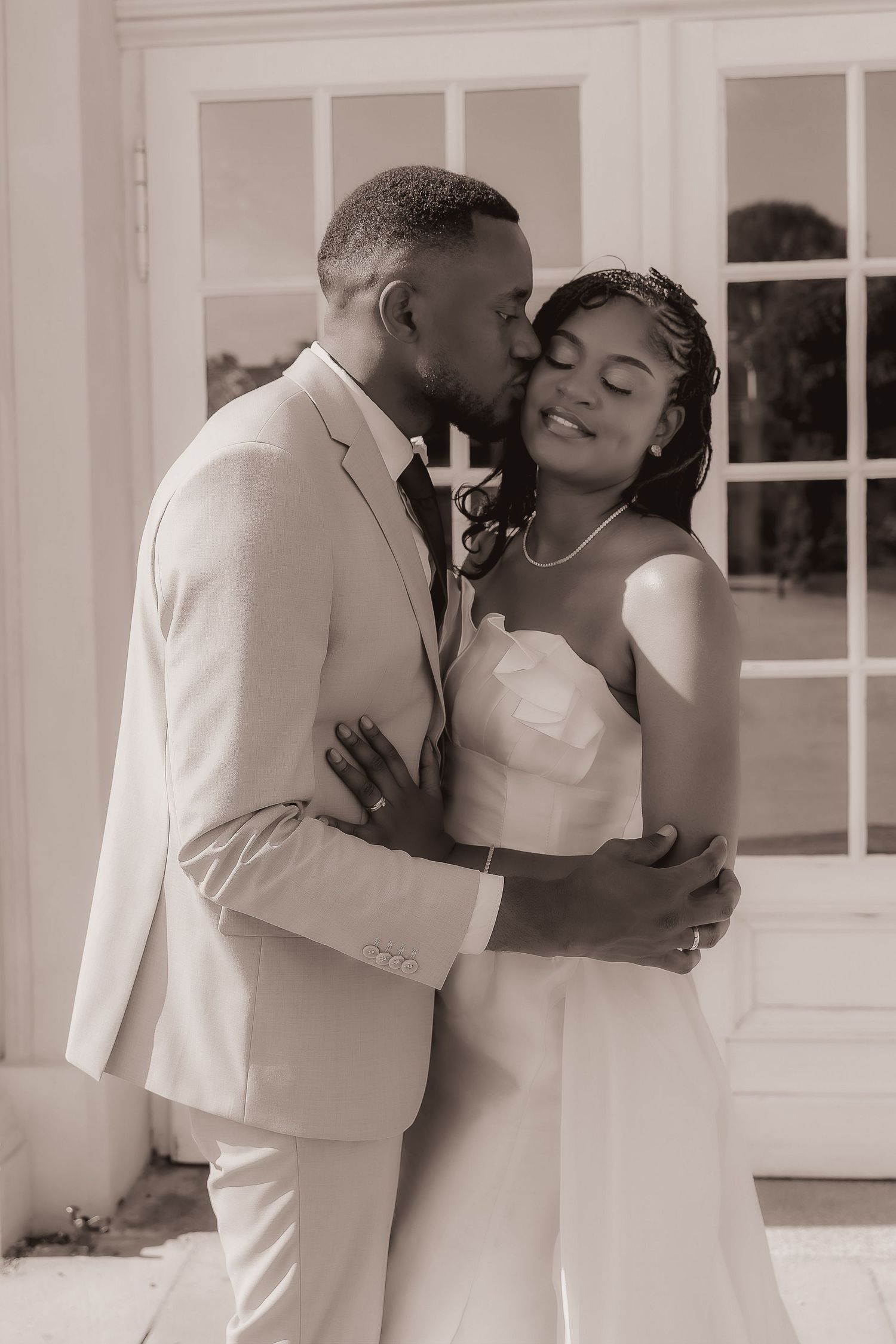 Romantic sepia-toned portrait of groom kissing brides cheek as she smiles with eyes closed outside.