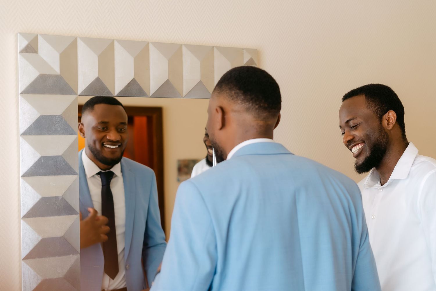 Three well-dressed Black men laughing and smiling together, one wearing a light blue suit with a dark tie.