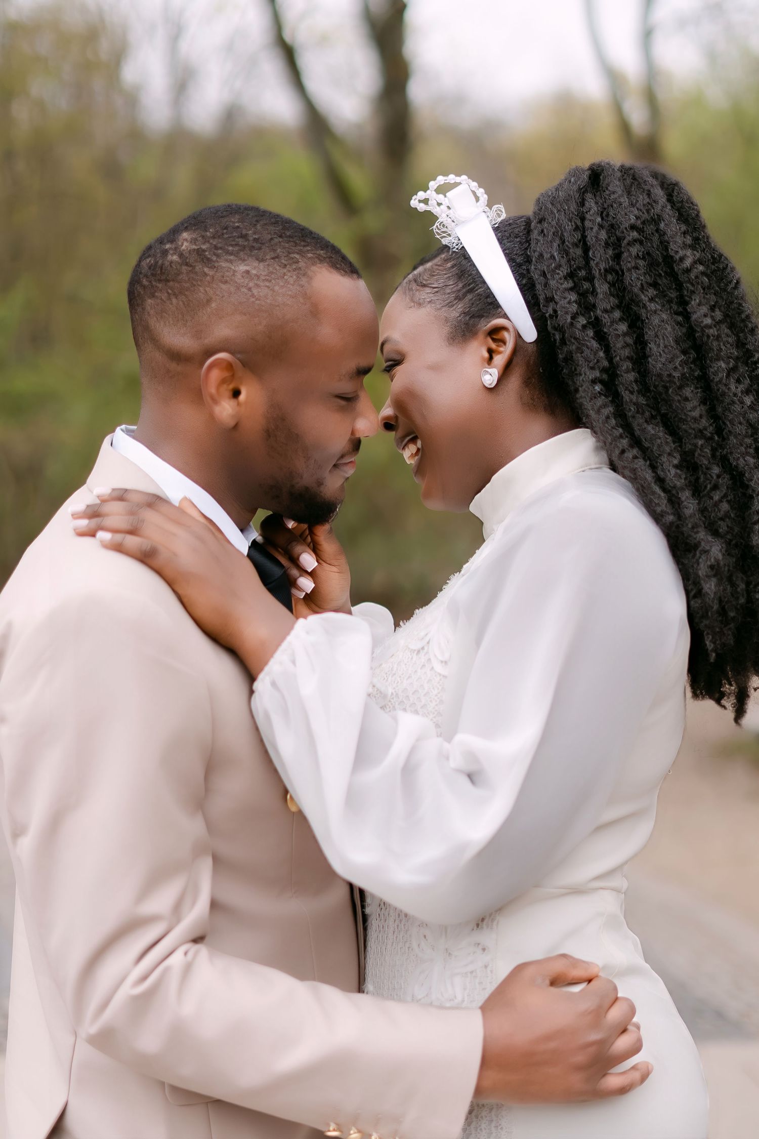 Close-up of Black bride and groom smiling forehead-to-forehead, bride wearing crystal tiara and white gown.