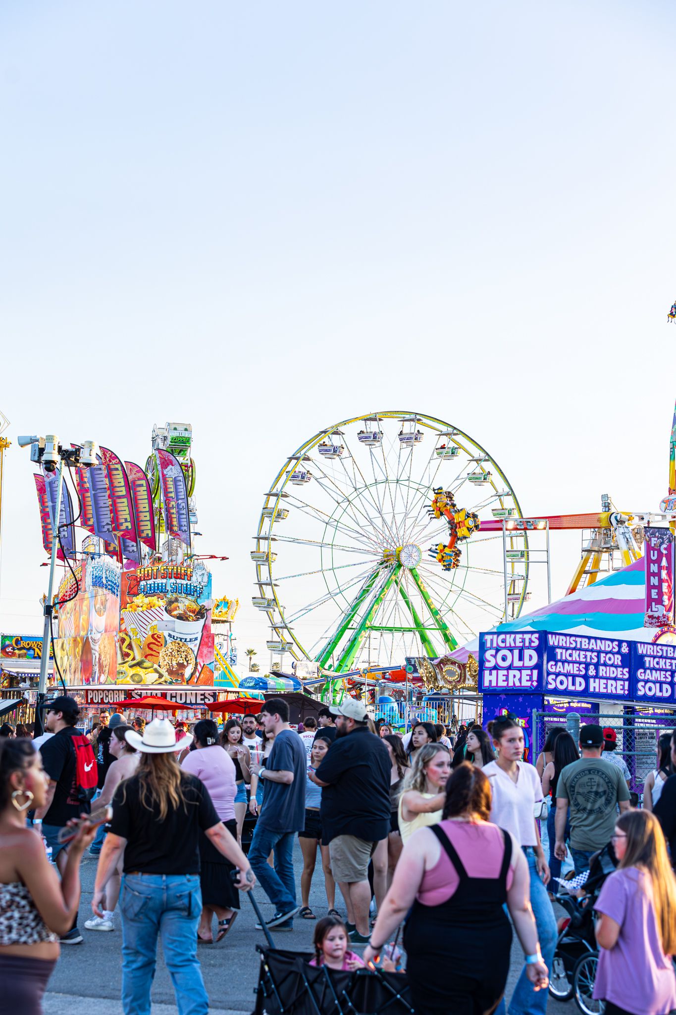 Crowds enjoy a lively county fair midway with a colorful Ferris wheel at dusk.
