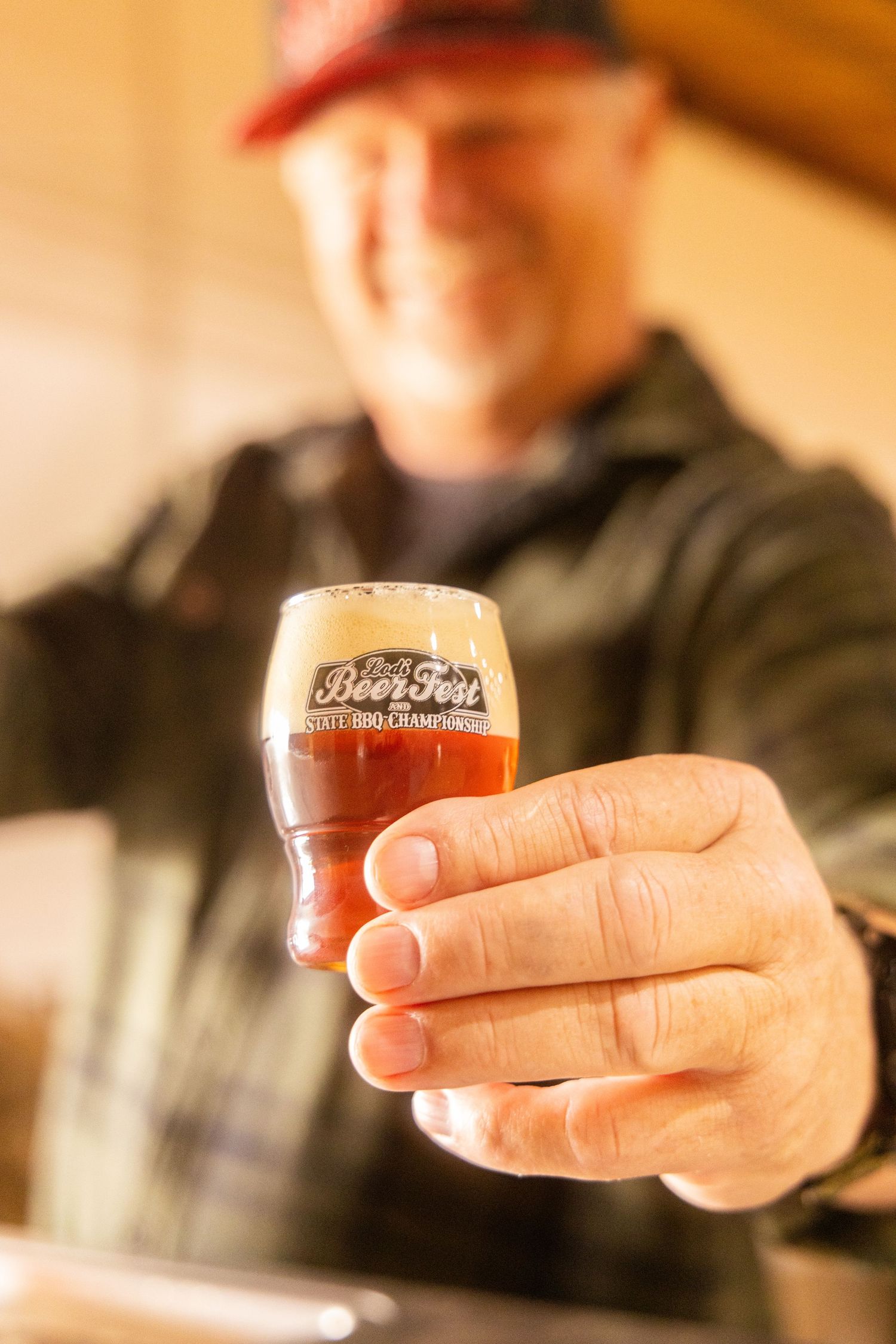 Man smiling and holding a craft beer glass from Beer Fest BBQ Championship toward the camera.