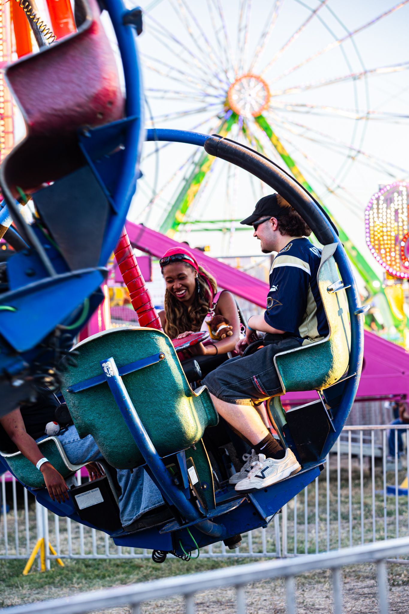 Two teens laugh together on a spinning carnival ride at a county fair.
