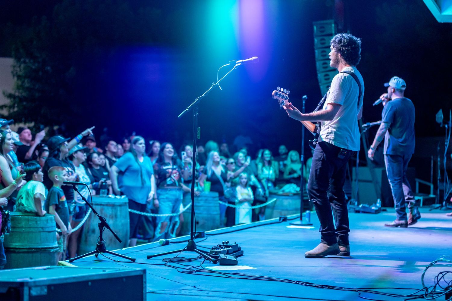 Live band performing on an outdoor stage with blue and green lights illuminating a large crowd.