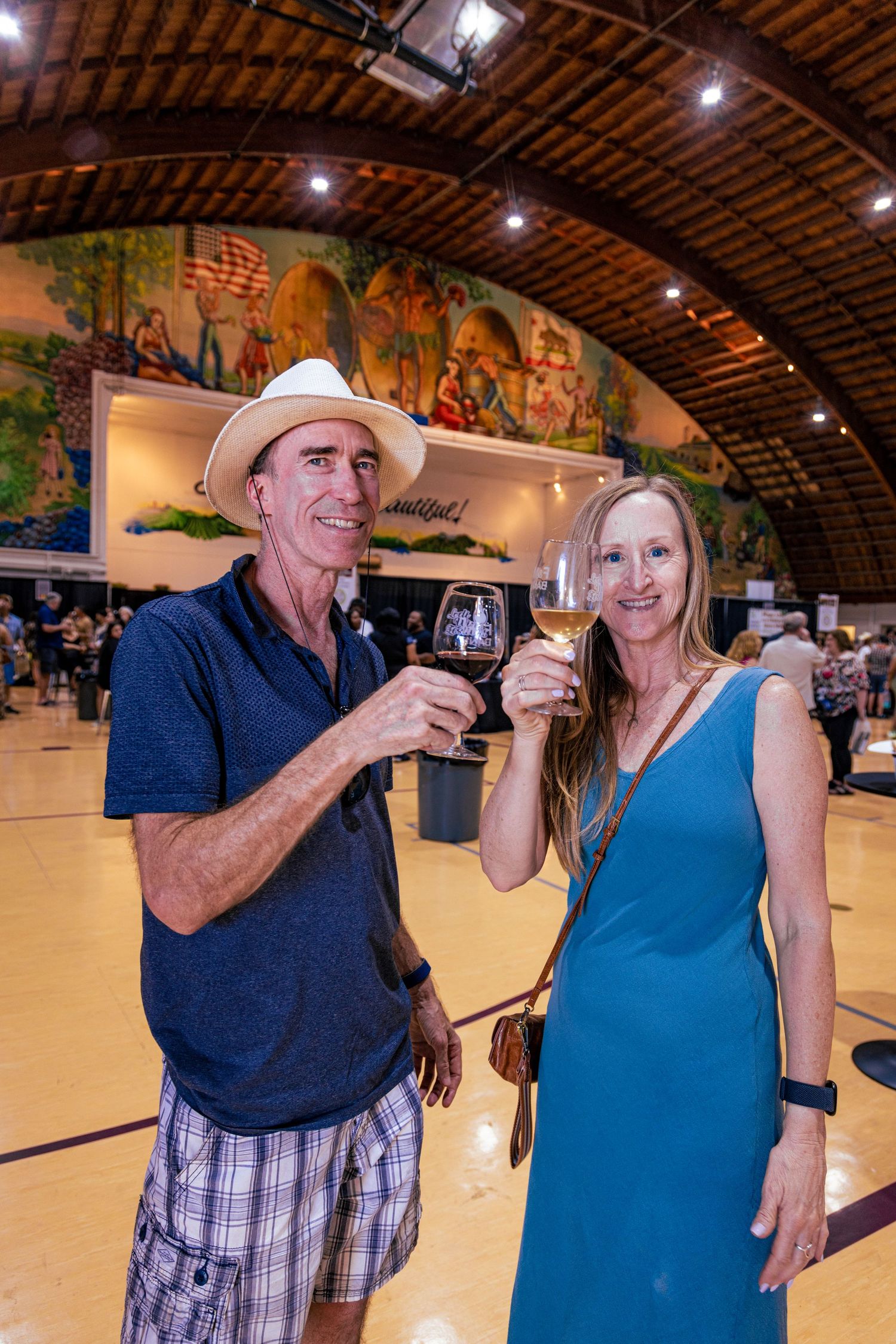 Couple toasting with wine glasses at an indoor wine festival beneath a decorative mural.