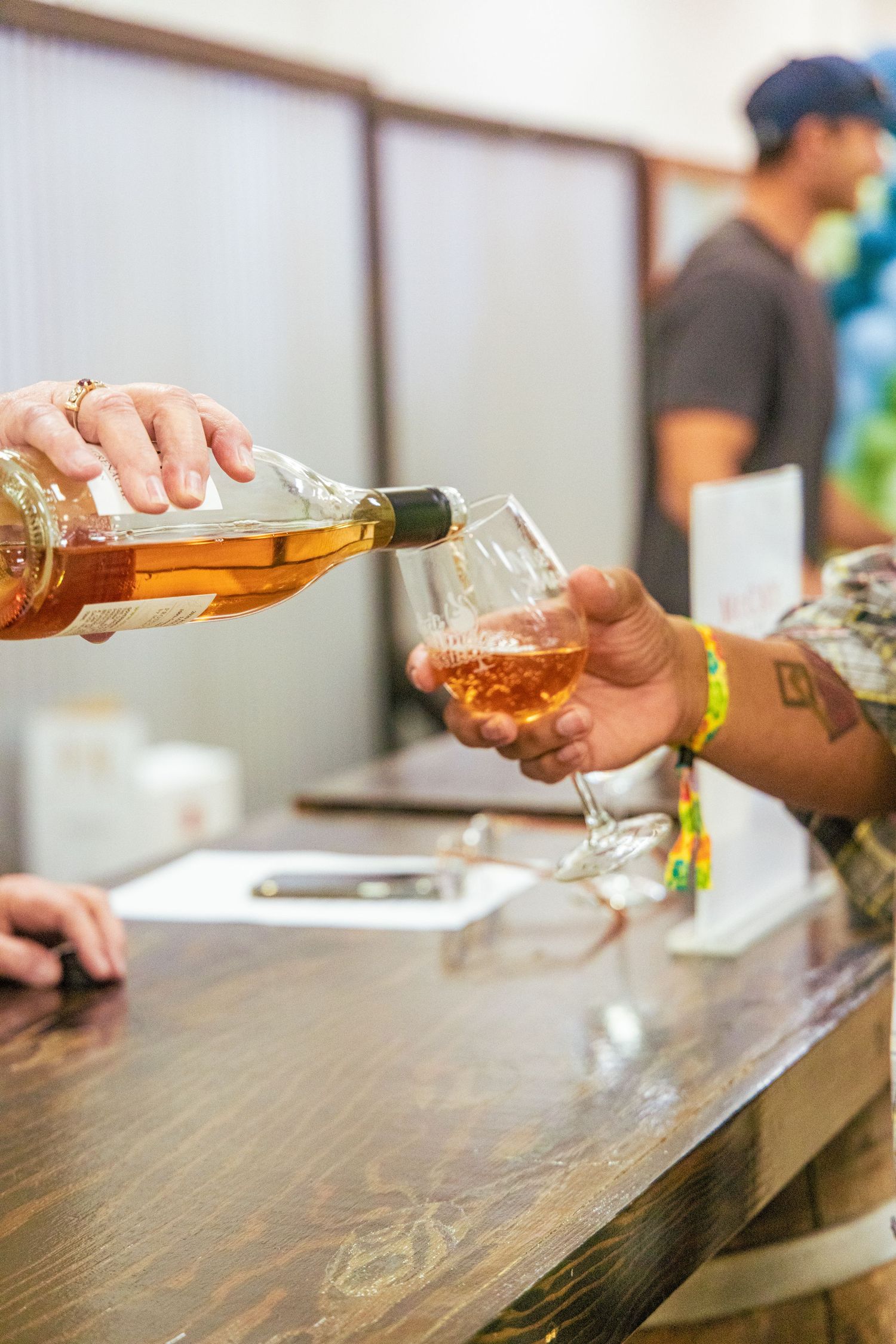 Rose wine being poured into a glass at a wine tasting bar with tattooed hand holding glass.
